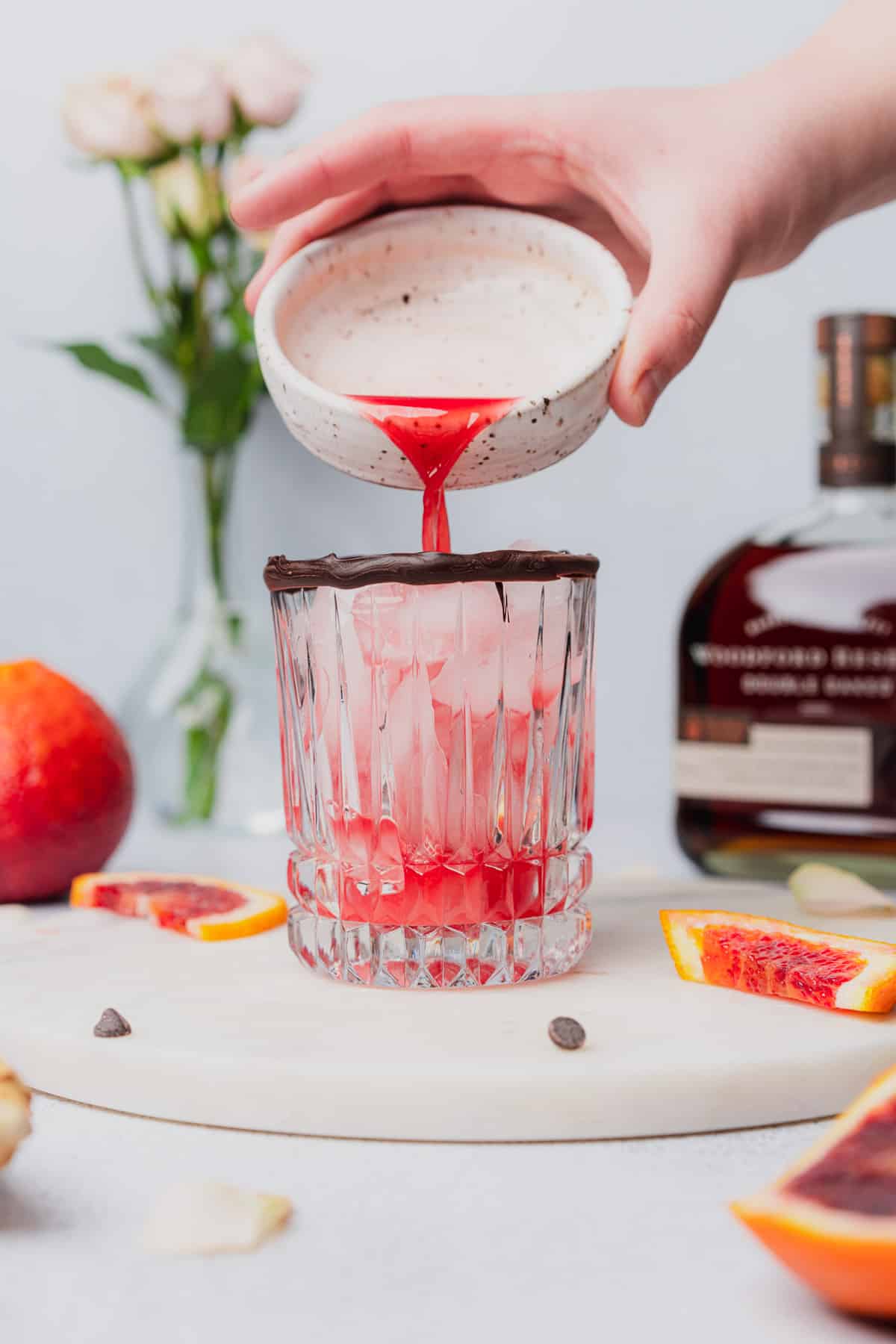 hand pouring blood orange juice into a cocktail glass with ice