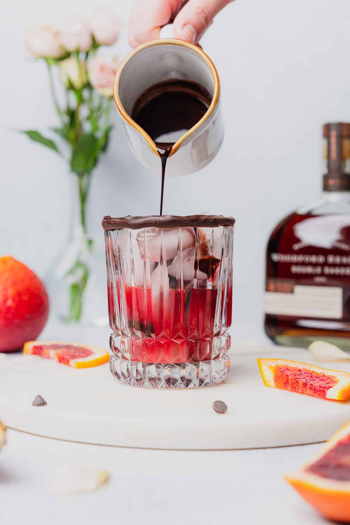 pouring in chocolate simple syrup to a glass full of blood orange juice 