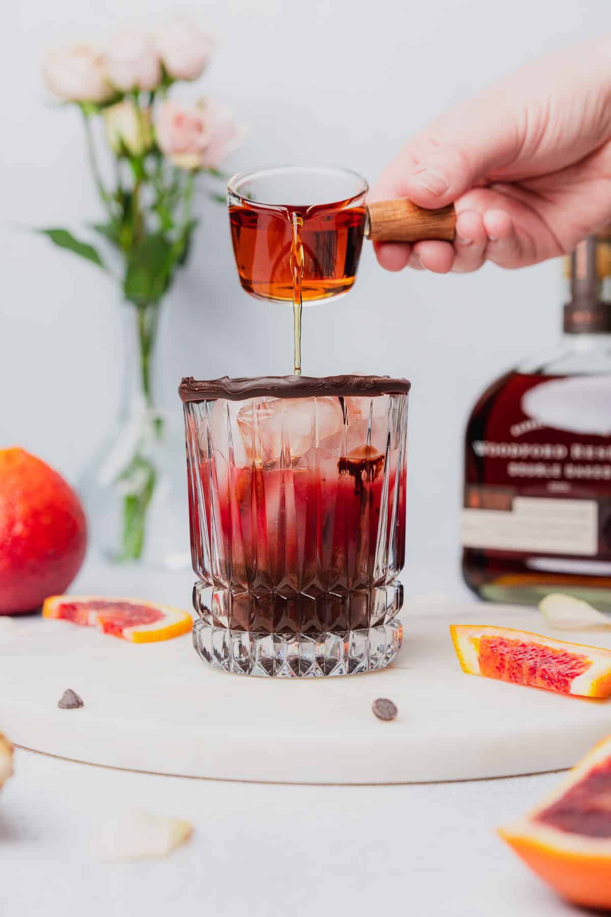 pouring bourbon into an ice filled glass with chocolate and blood orange