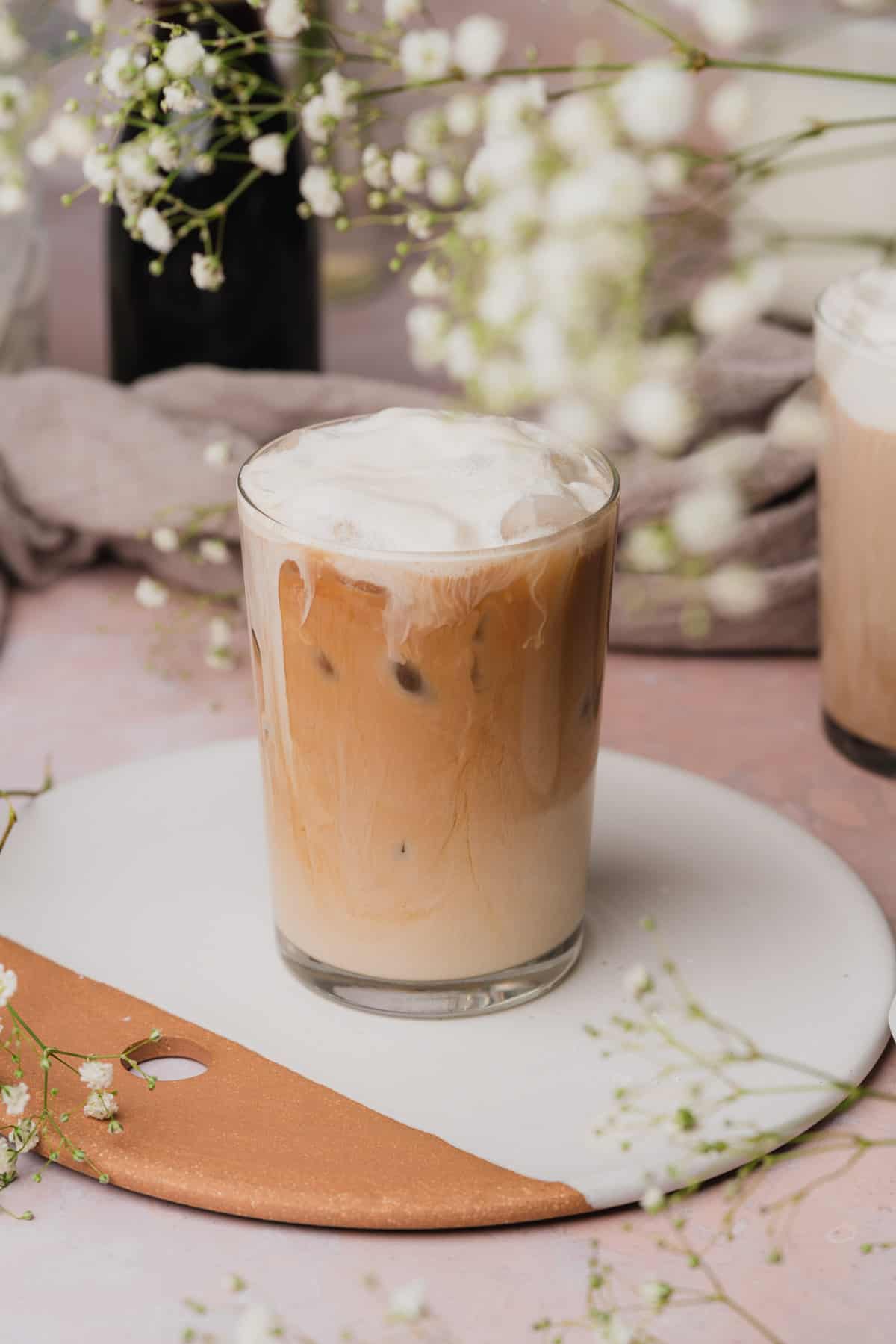 photo of an iced sweet cream cold foam coffee surrounded by small white baby's breath flowers.