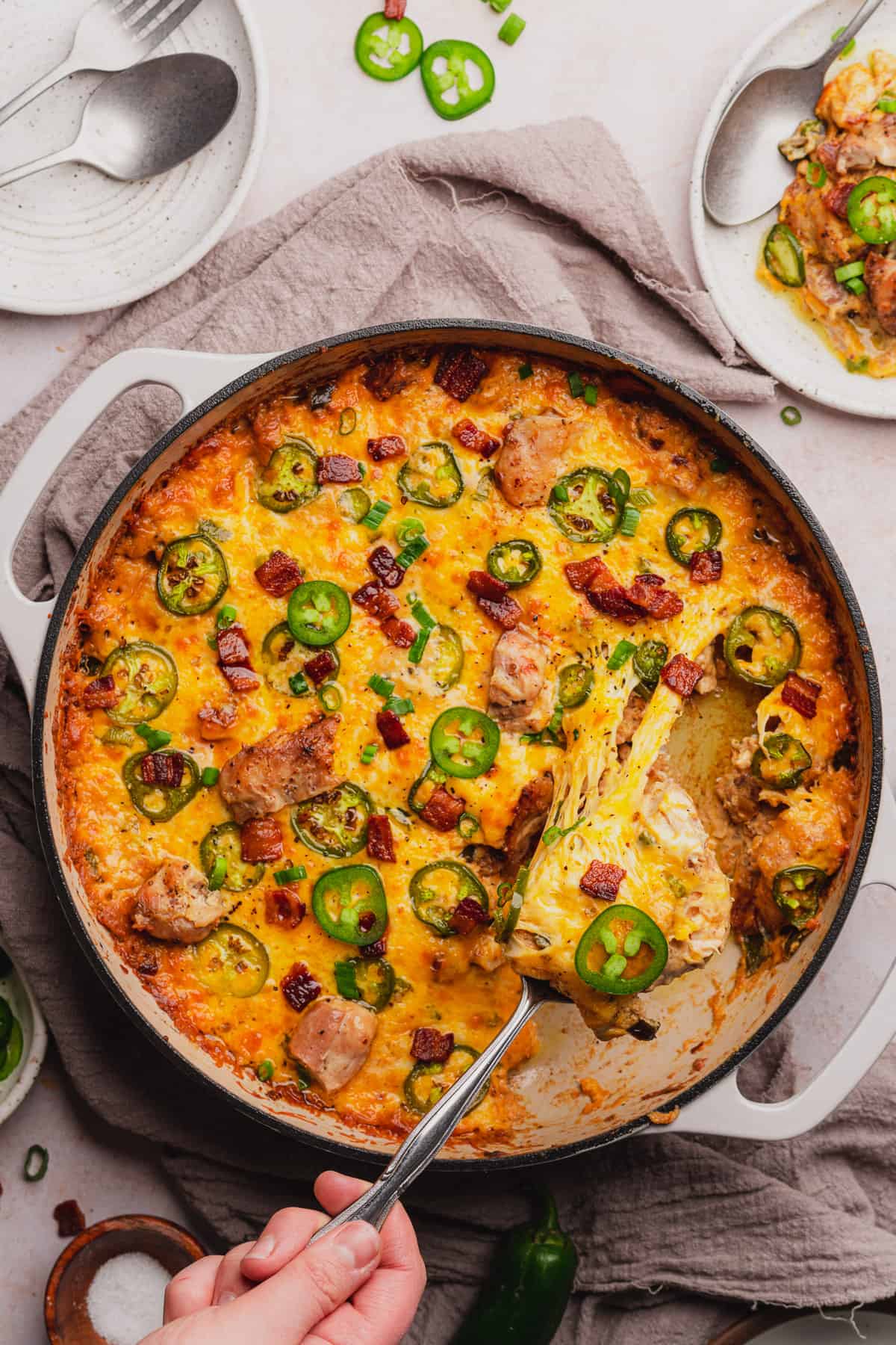 hand pulling cheesy jalapeno popper chicken from a skillet