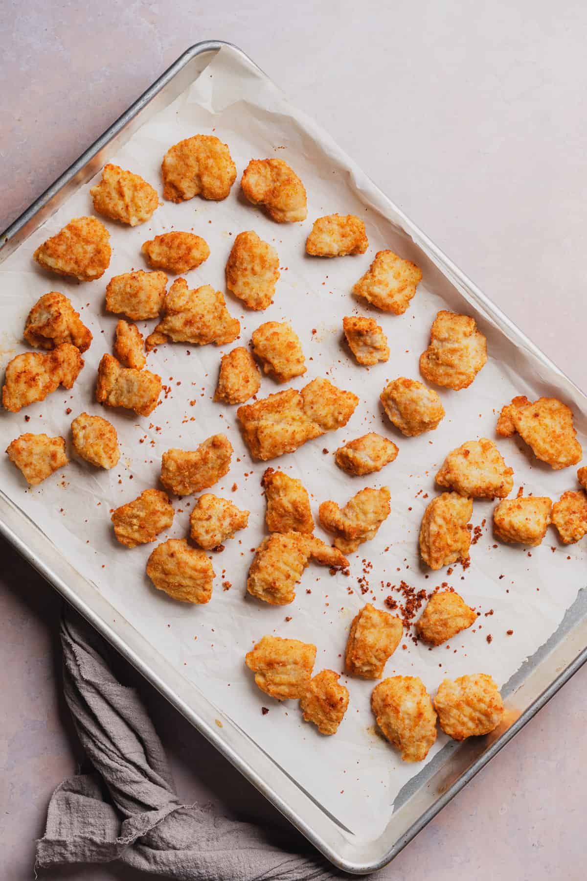 crispy golden brown chicken nuggets on a parchment lined baking sheet