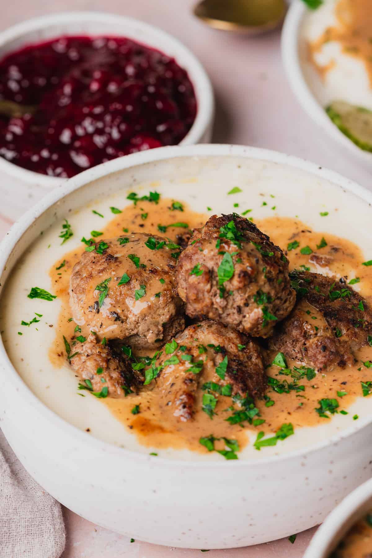 bowl full of creamy mashed turnips and keto swedish meatballs with lingonberry sauce in the background.