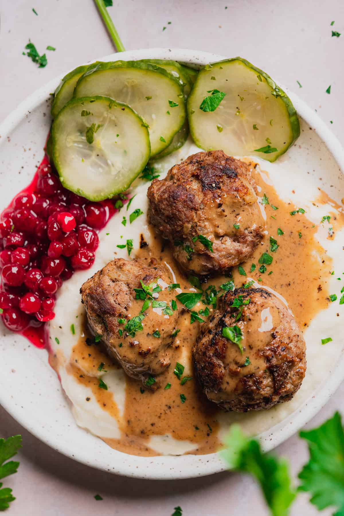 keto swedish meatballs on a plate with mashed turnips, lingonberry jam, cucumber salad, and parsley. 