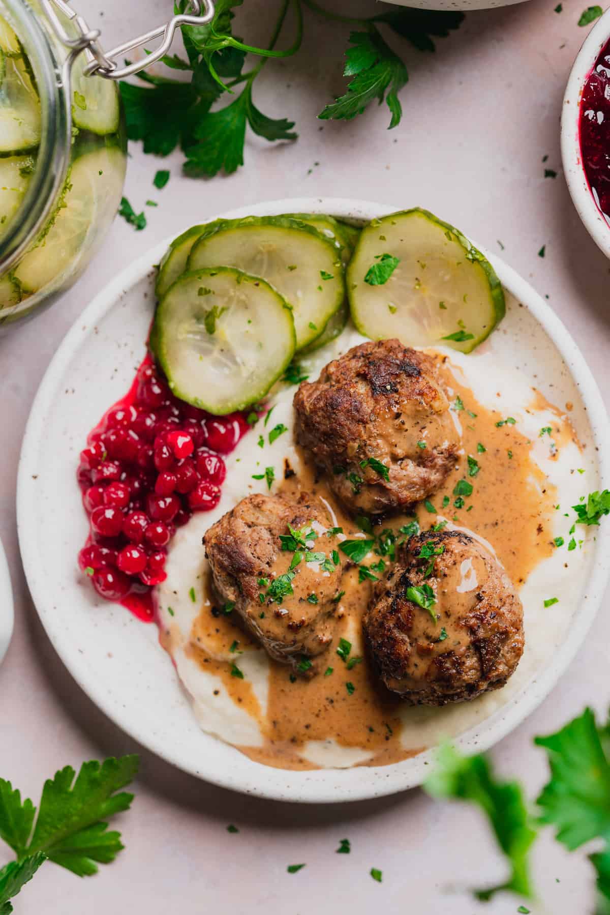 plate of swedish meatballs and gravy with mashed turnips, cucumber salad and lingonberry sauce. 
