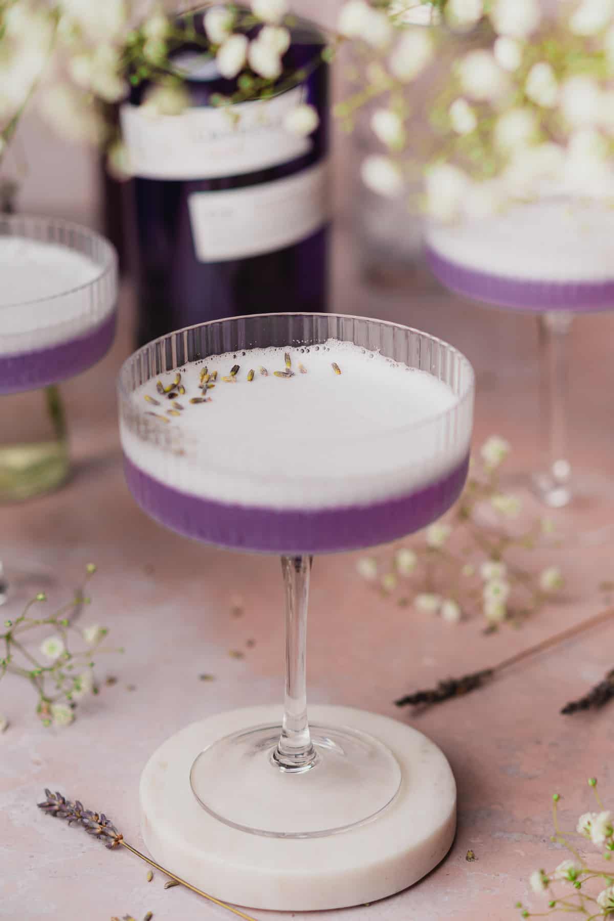 super pretty close up shot of a lavender gin cocktail with foamy egg white topping.