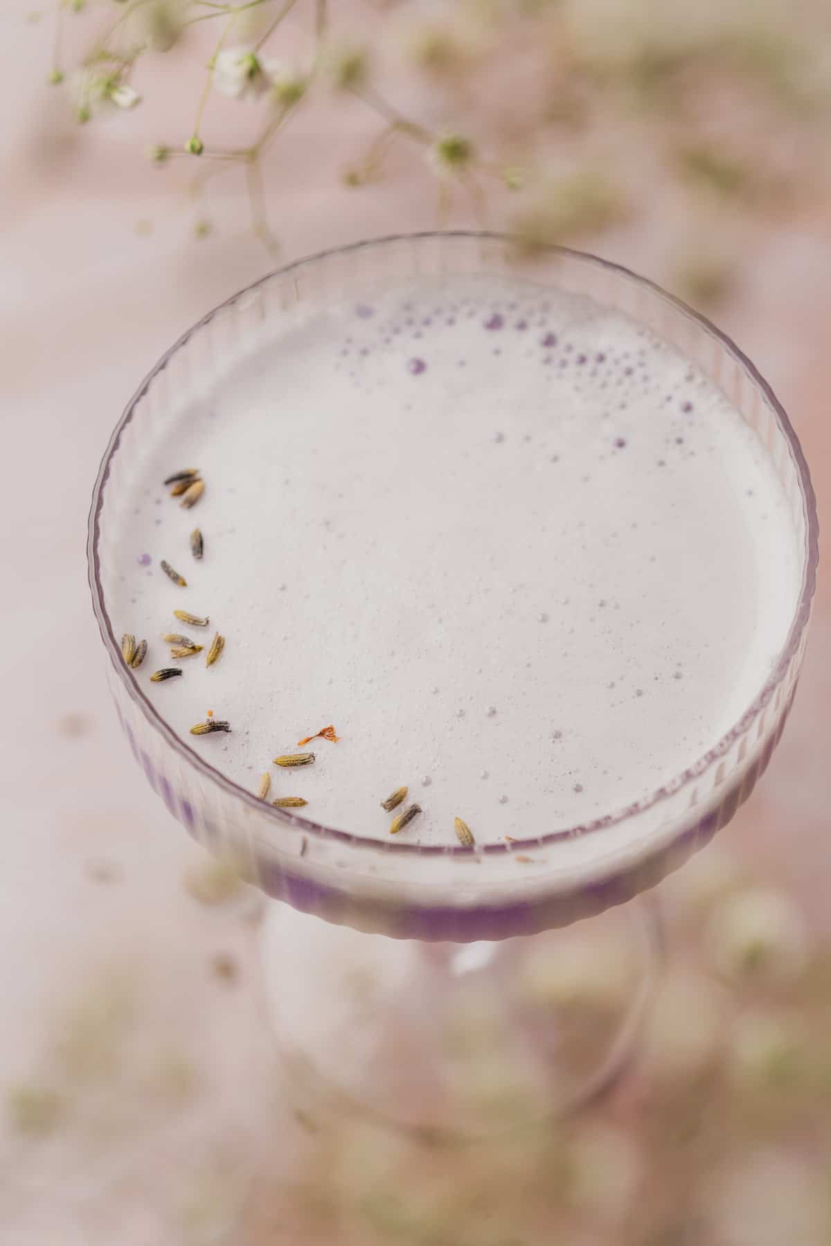 close up shot of the top of a lavender gin cocktail recipe with a foamy egg white top and dried lavender buds 