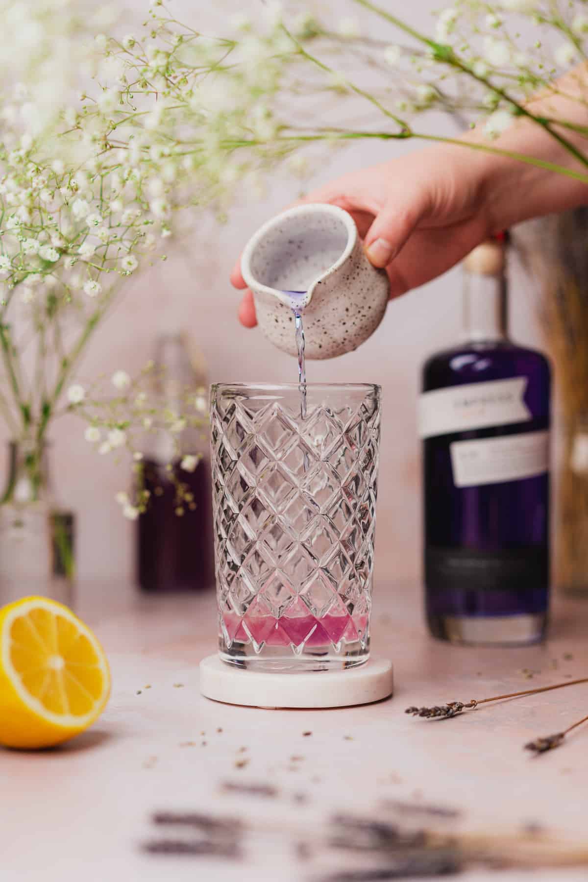hand pouring empress gin into a cocktail shaker and watching the liquid turn into a pretty purple color 