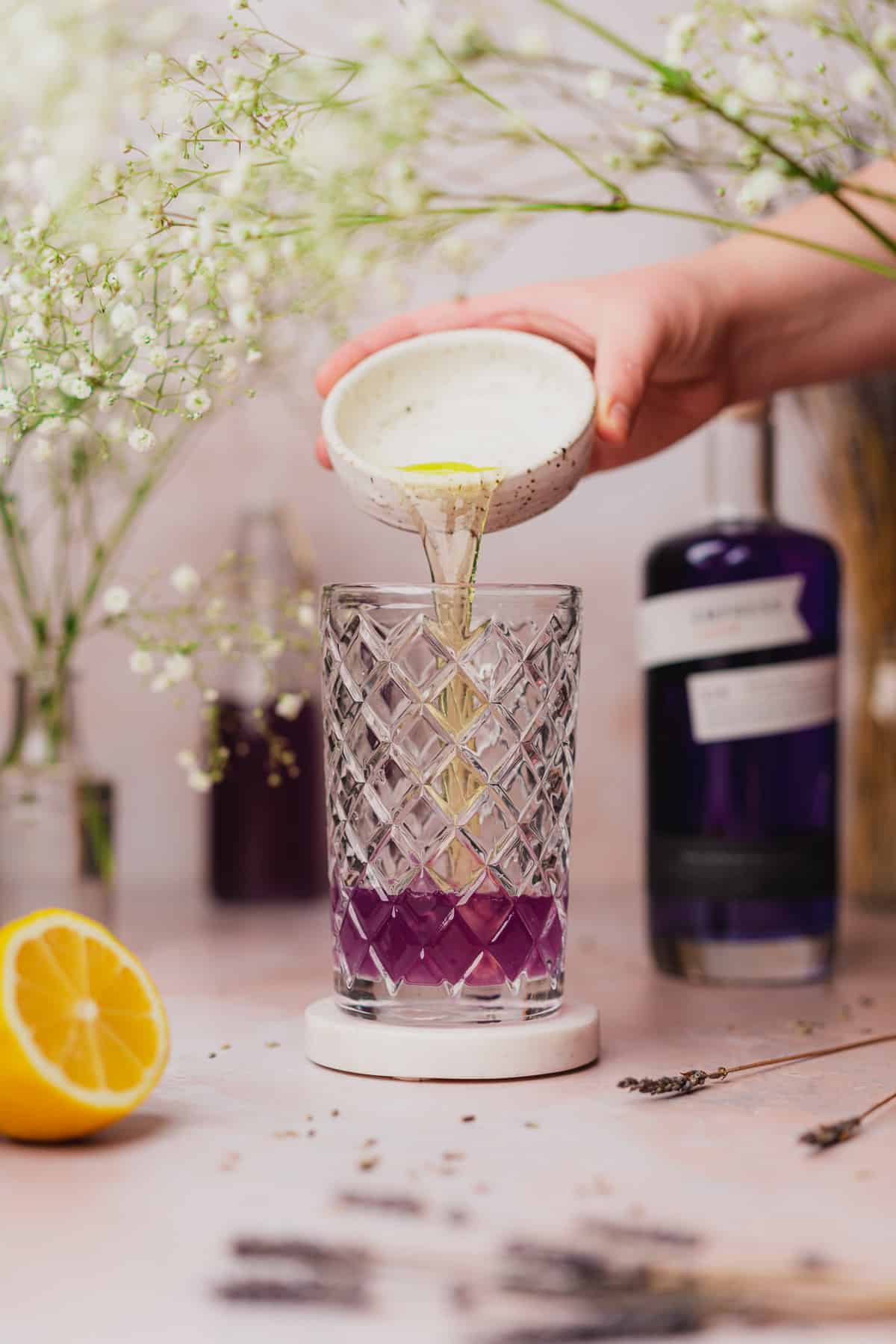 hand pouring an egg white into a cocktail shaker with purple gin and lemon juice 