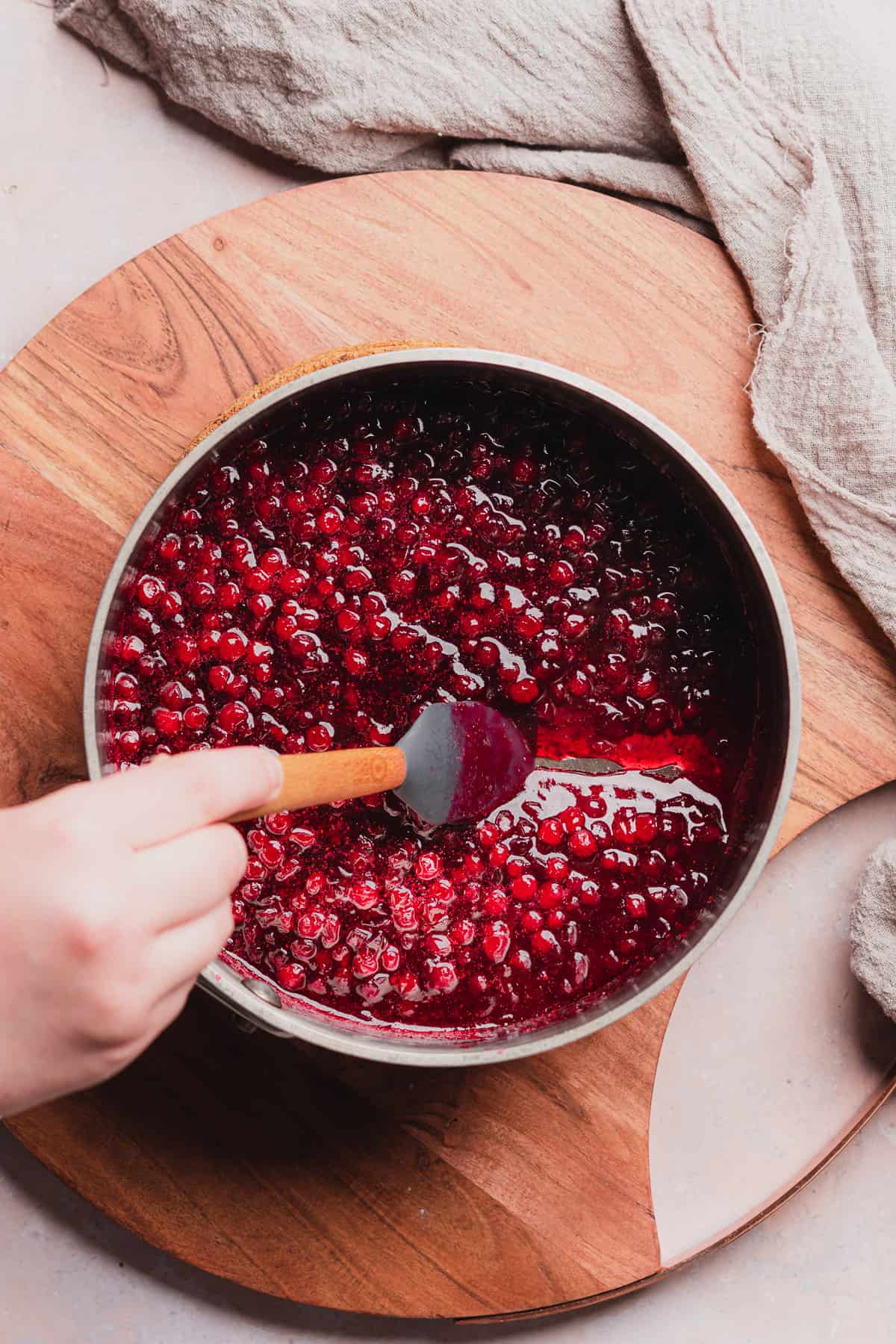 hand dragging a rubber spatula along the bottom of a saucepan with lingonberry sauce inside to show that the sauce has thickened. 