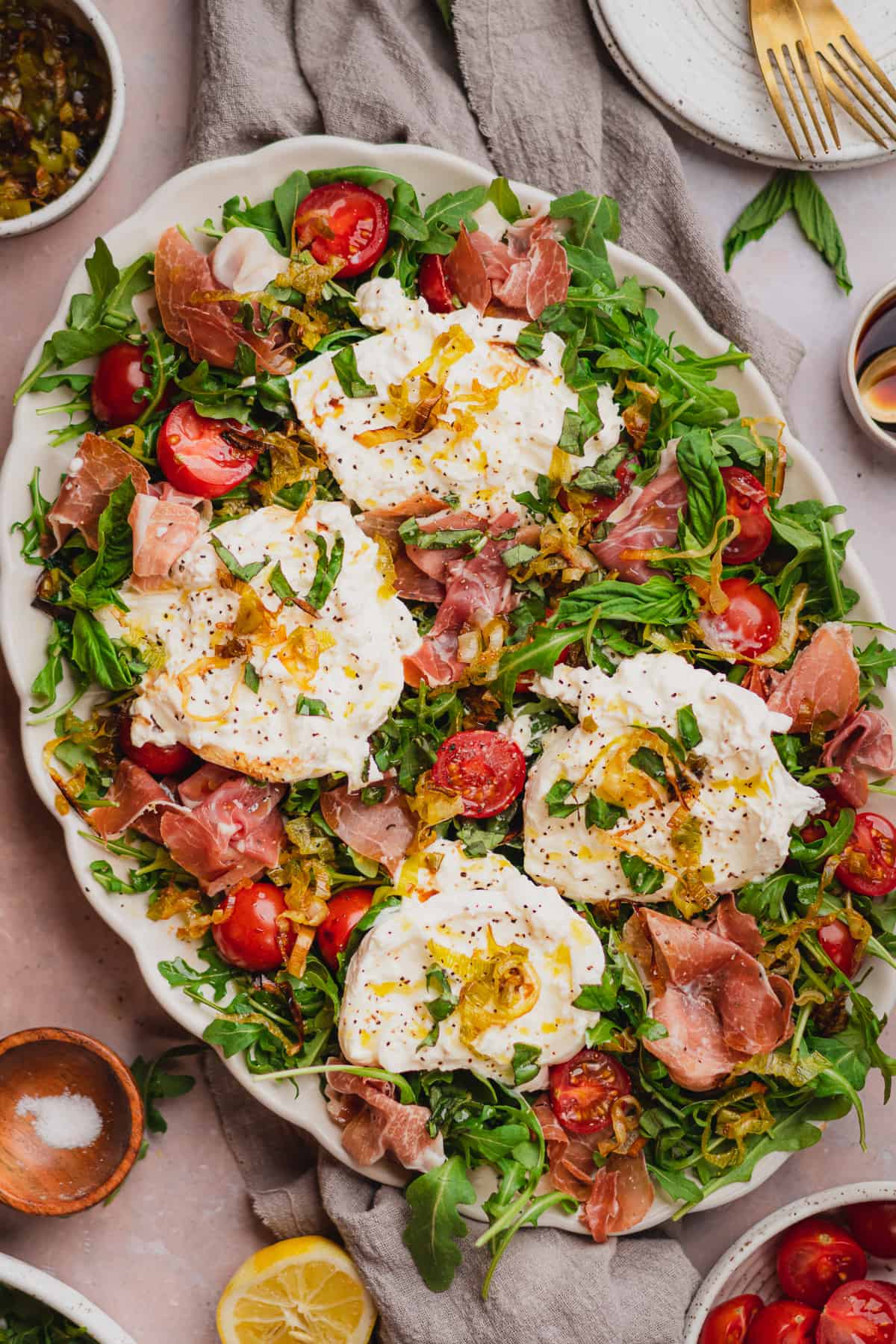 flat lay scene of a burrata and prosciutto salad with tomatoes, basil, and fried leeks.