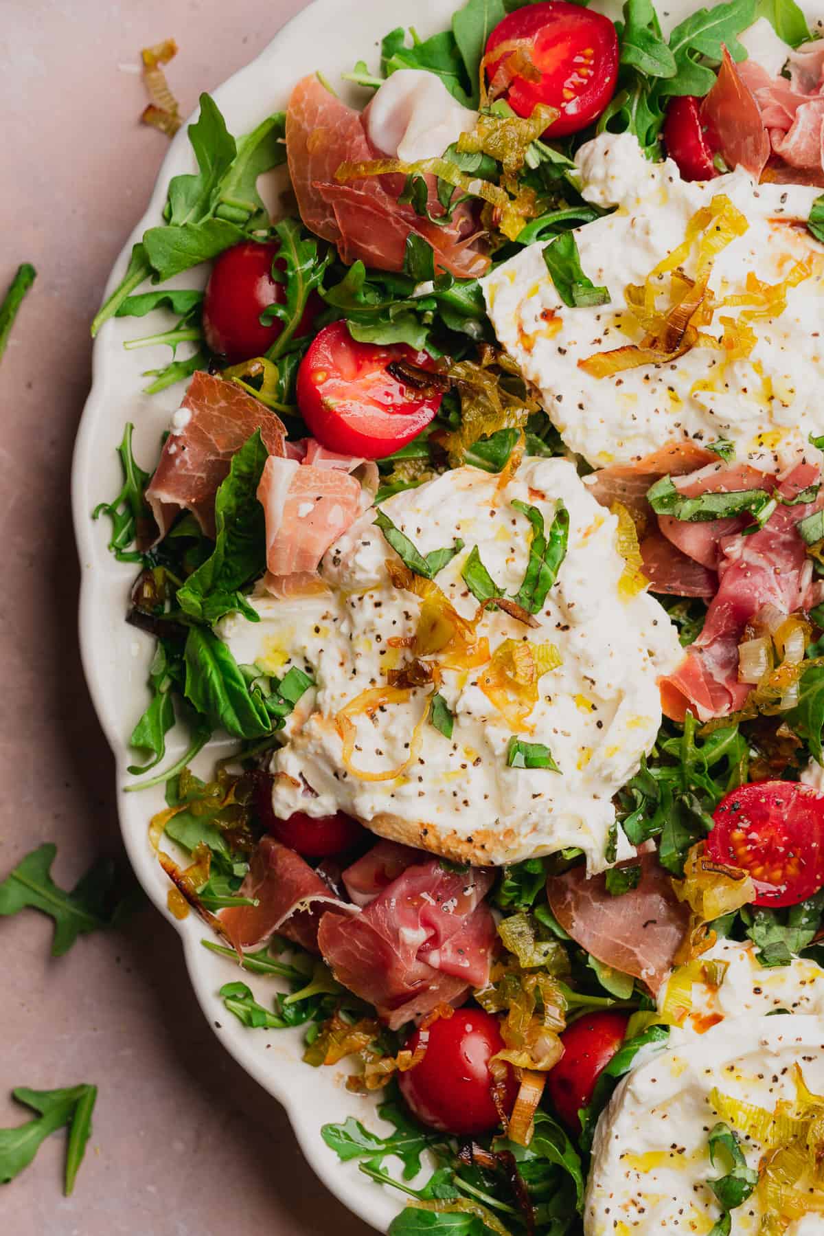 close up shot of burrata and prosciutto arugula salad with tomatoes, basil, and fried leeks. 