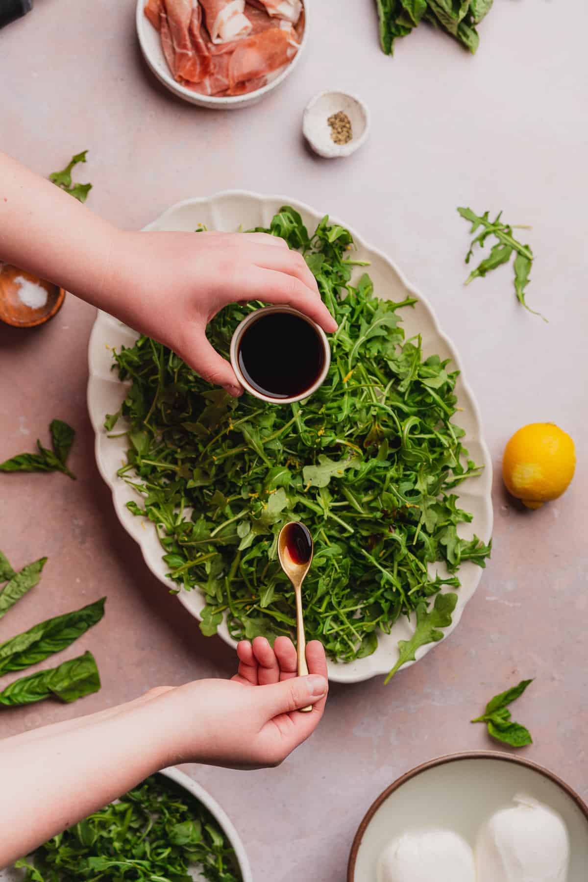 hand drizzling balsamic vinegar over top of an arugula salad.