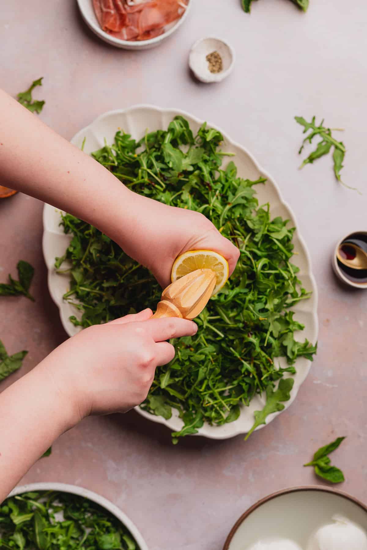 hand squeezing fresh lemon juice over top of an arugula salad. 
