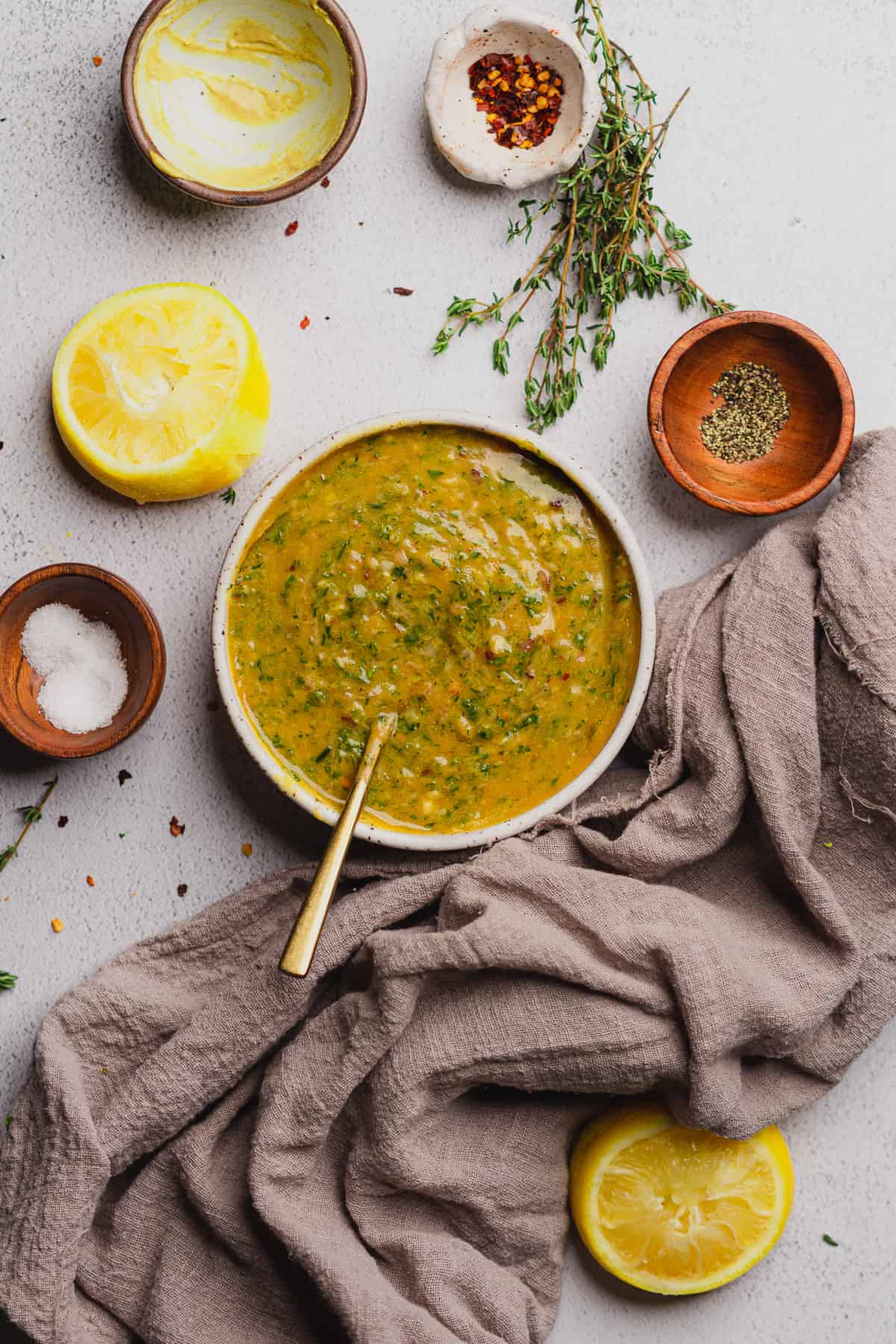 bowl full of cowboy butter dipping sauce with a grey linen towel nearby, alongside black pepper, fresh thyme, lemon, and kosher salt. 