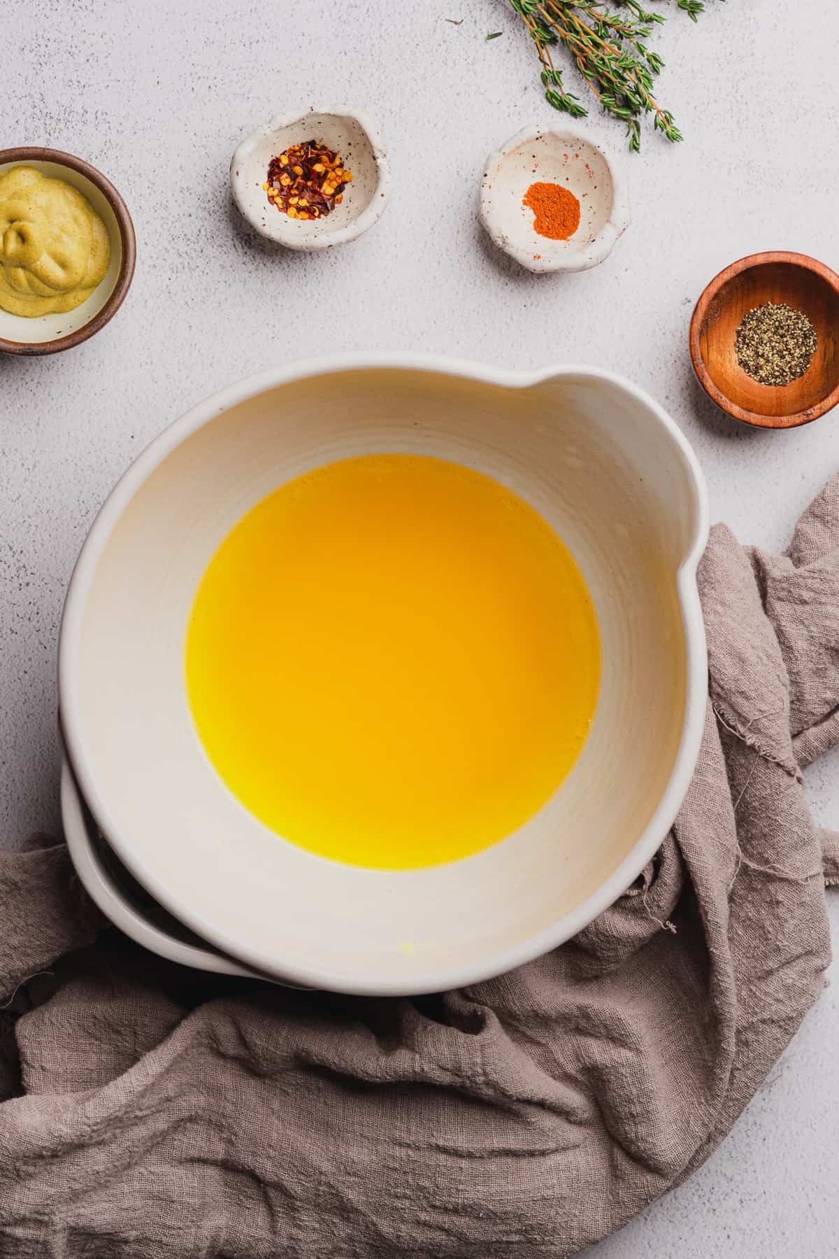 melted butter in a ceramic white mixing bowl surrounded by seasonings.  