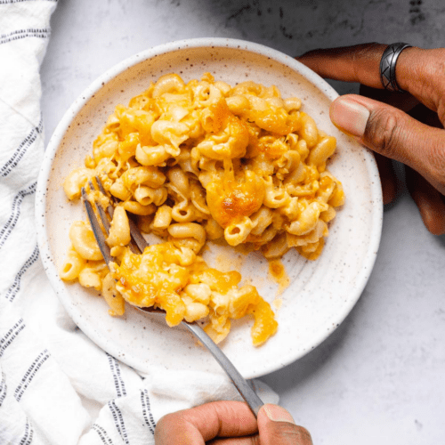 Keto mac and cheese on white plate held by beautiful black hands on white backdrop