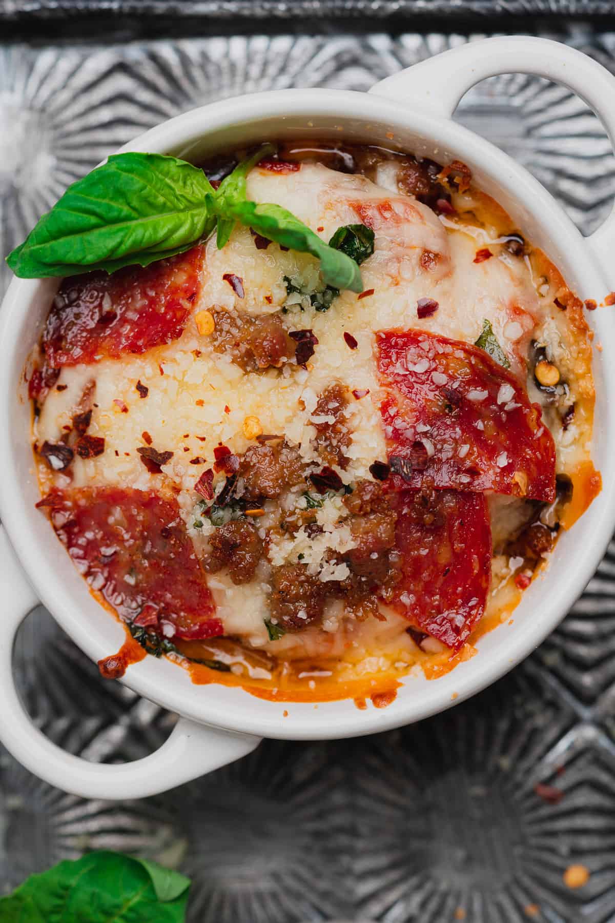 cheesy pizza bowl in a white ramekin topped with fresh basil and red pepper flakes. 