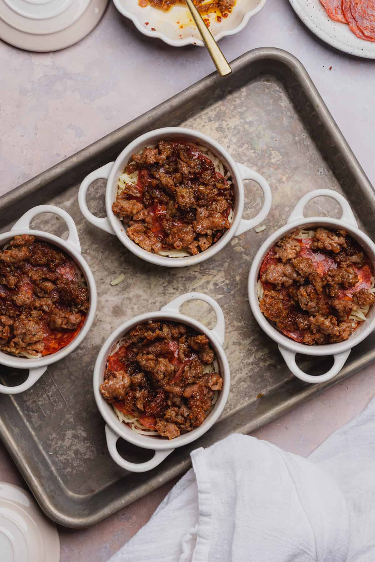 ramekins with cooked italian sausage and pepperonis in them on a baking sheet. 