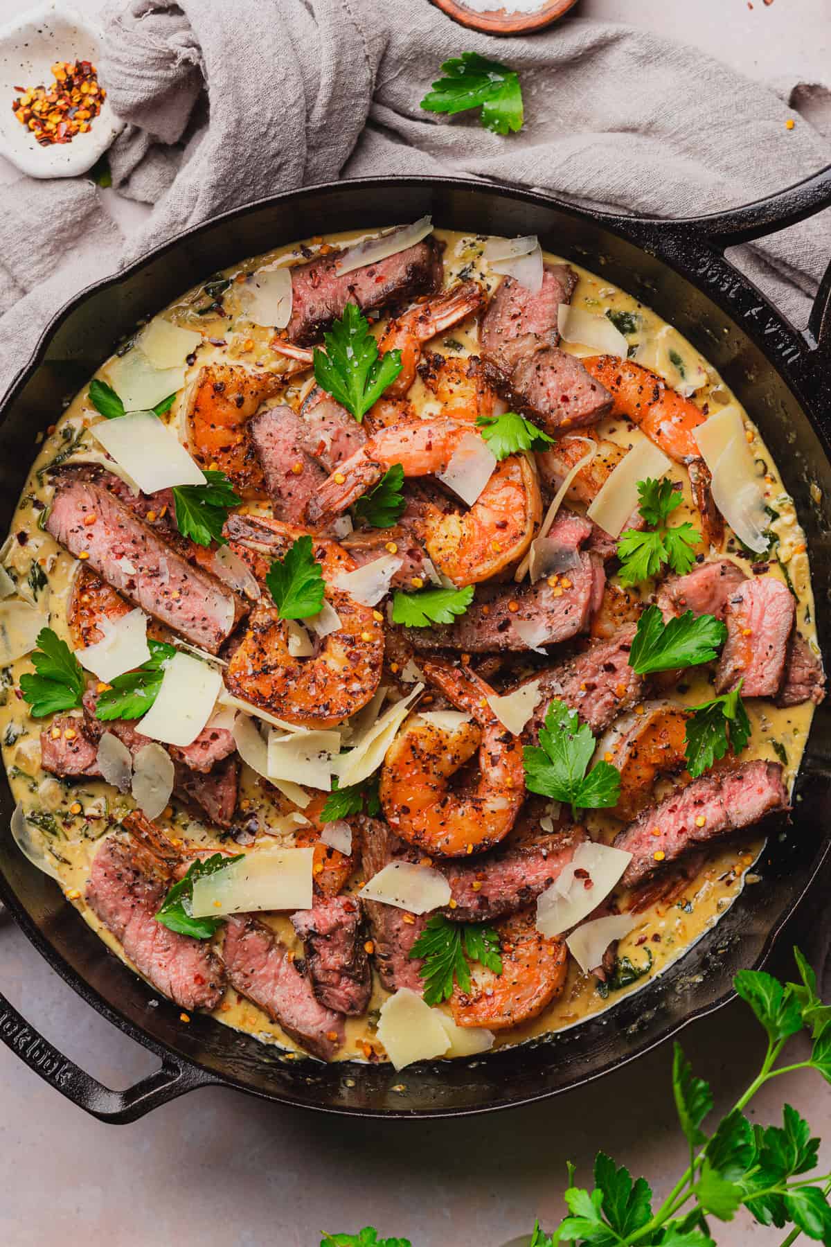 steak and seafood recipe with creamy parmesan sauce in a cast iron skillet. 