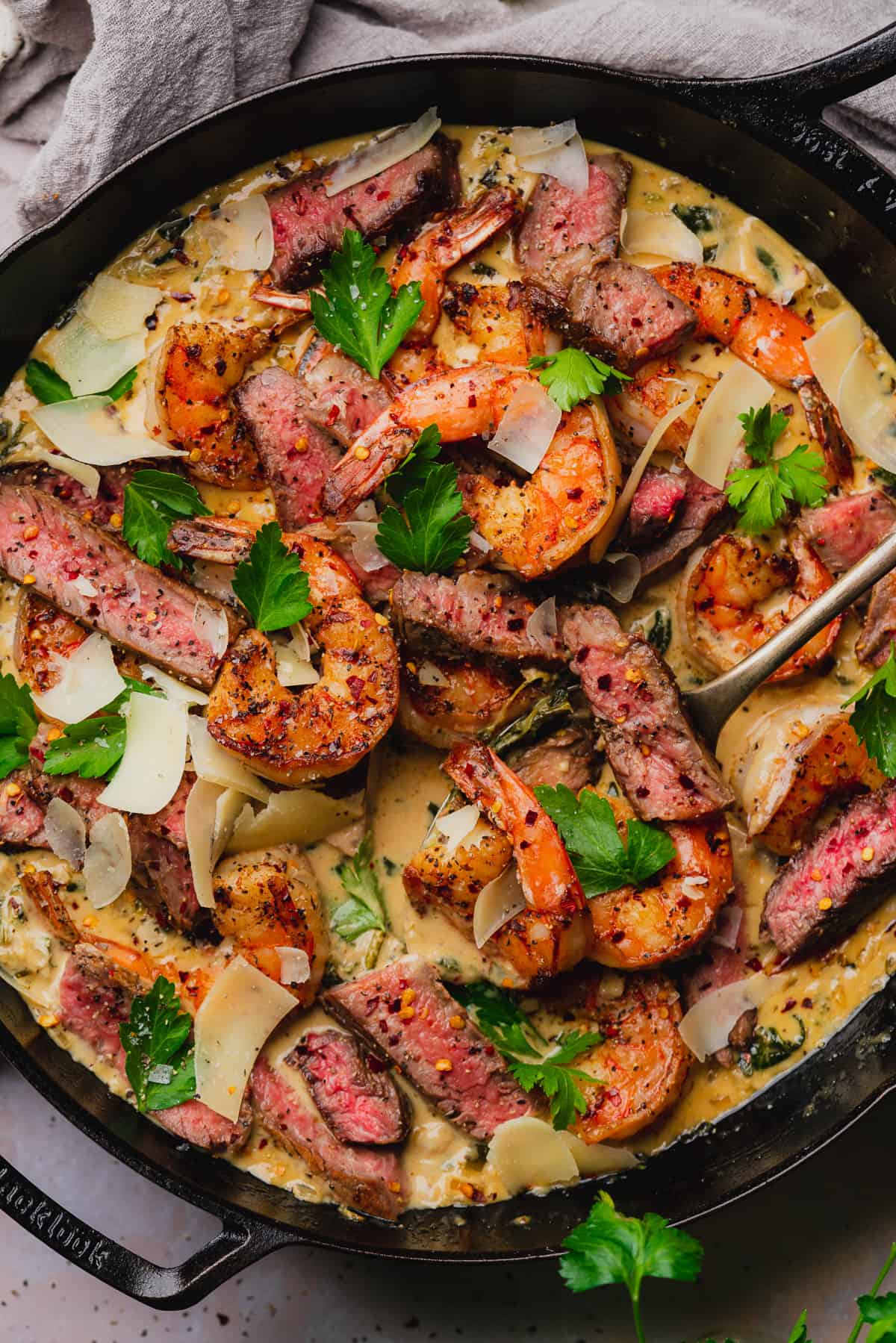 close up and delicious shot of a steak and seafood skillet with garlic parmesan cream sauce, fresh parsley, and parmesan flakes. 