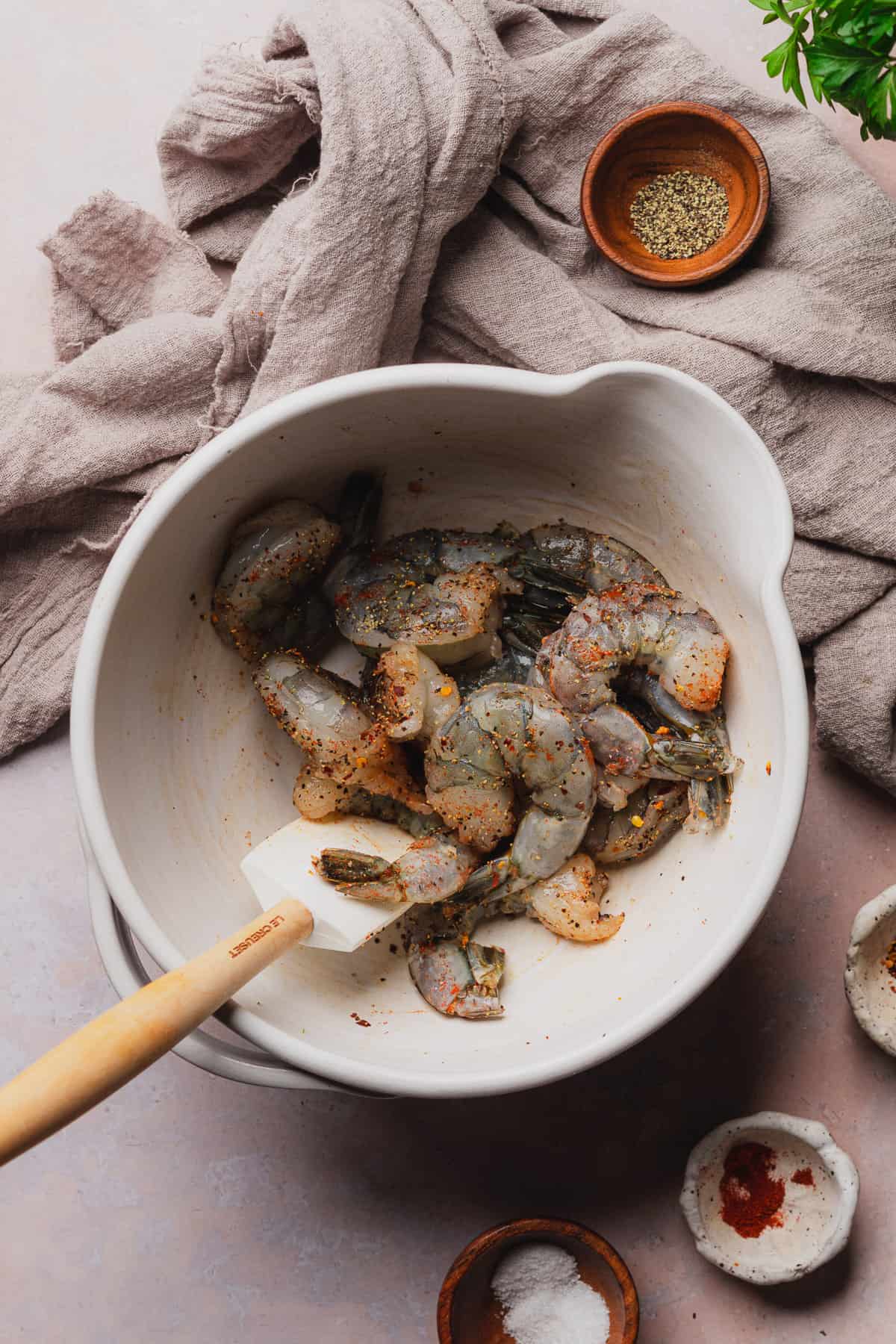 seasoning shrimp with salt, pepper, red pepper flakes, and smoked paprika in a bowl. 