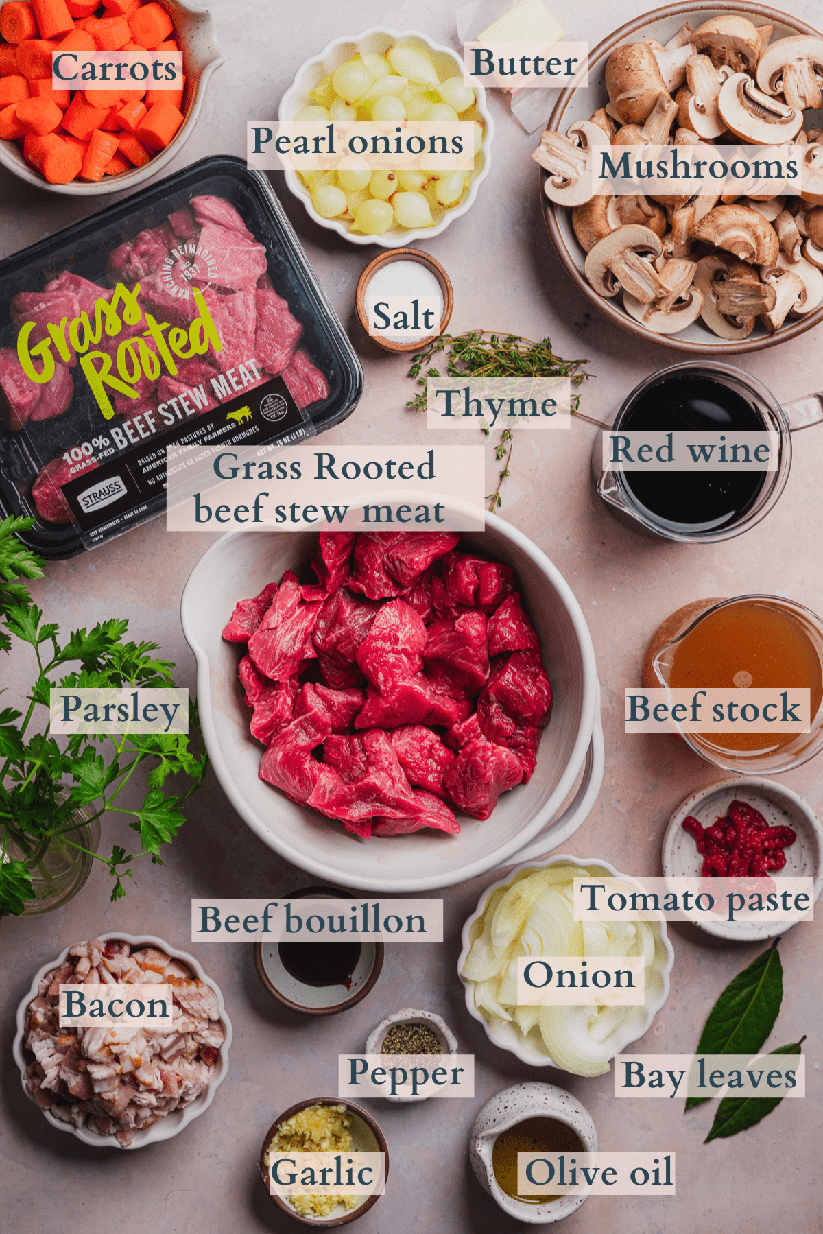 beef bourguignon recipe ingredients including carrots, pearl onions, onions, mushrooms, garlic, thyme, parsley, salt, pepper, beef stock, red wine, beef bouillon, butter, olive oil, beef stew meat, tomato paste, bay leaves, and bacon with text to denote each ingredient.  