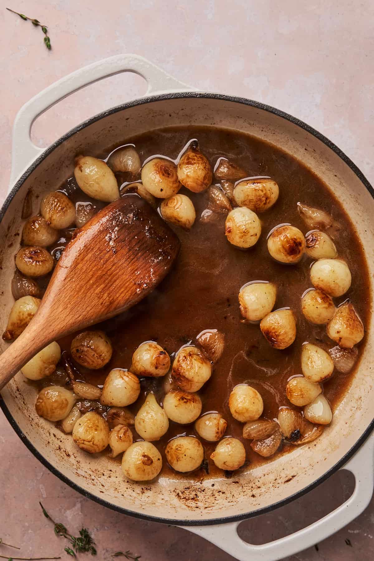 pearl onions in a skillet with a wooden spoon being caramelized. 