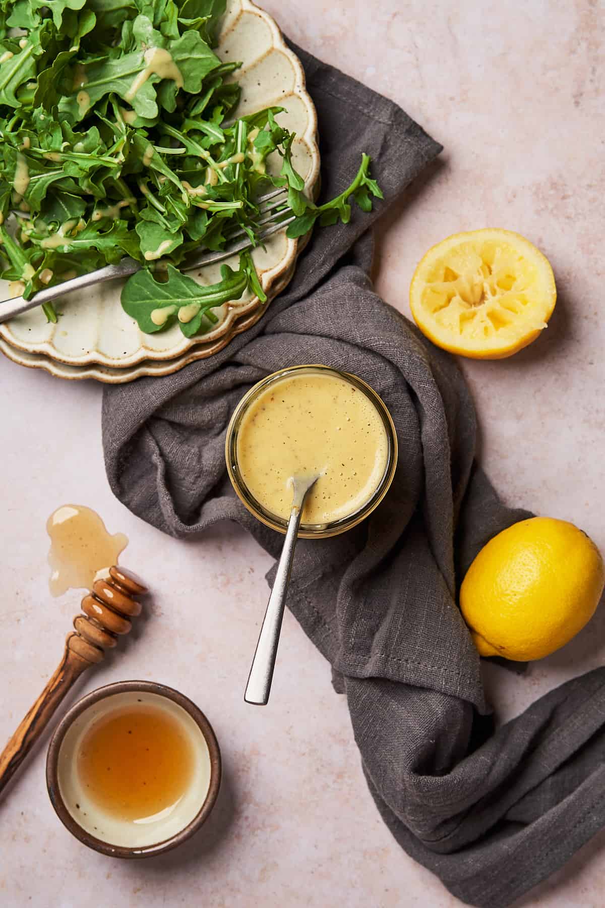 flat lay shot of honey lemon vinaigrette with lemon, a side salad and a honey dripper close by. 