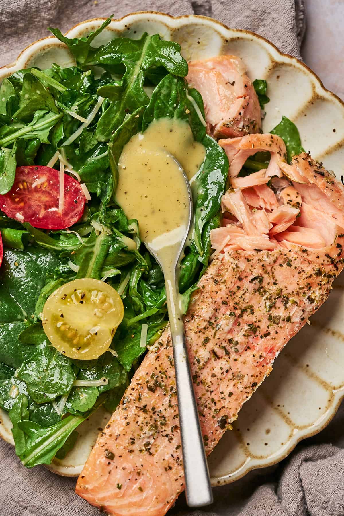spoonful of honey lemon vinaigrette dressing on top of a simple arugula and spinach salad, with a side of salmon. 