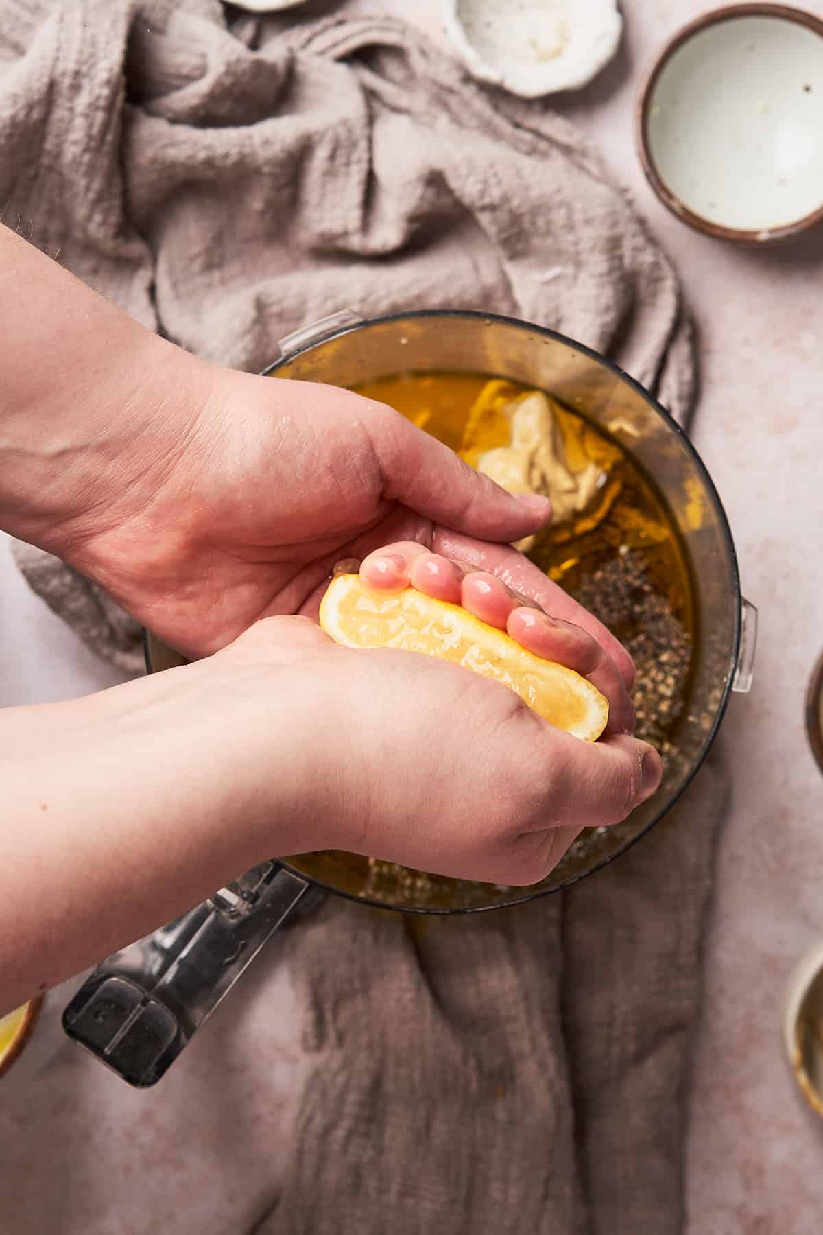 hand squeezing a lemon into a food processor to make a honey lemon dressing. 