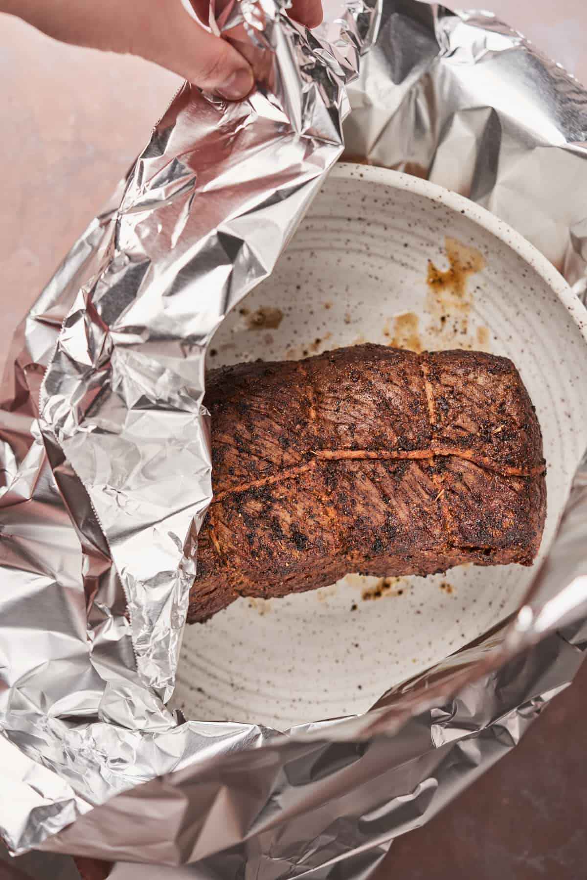 wrapping a beef roast in aluminum foil.