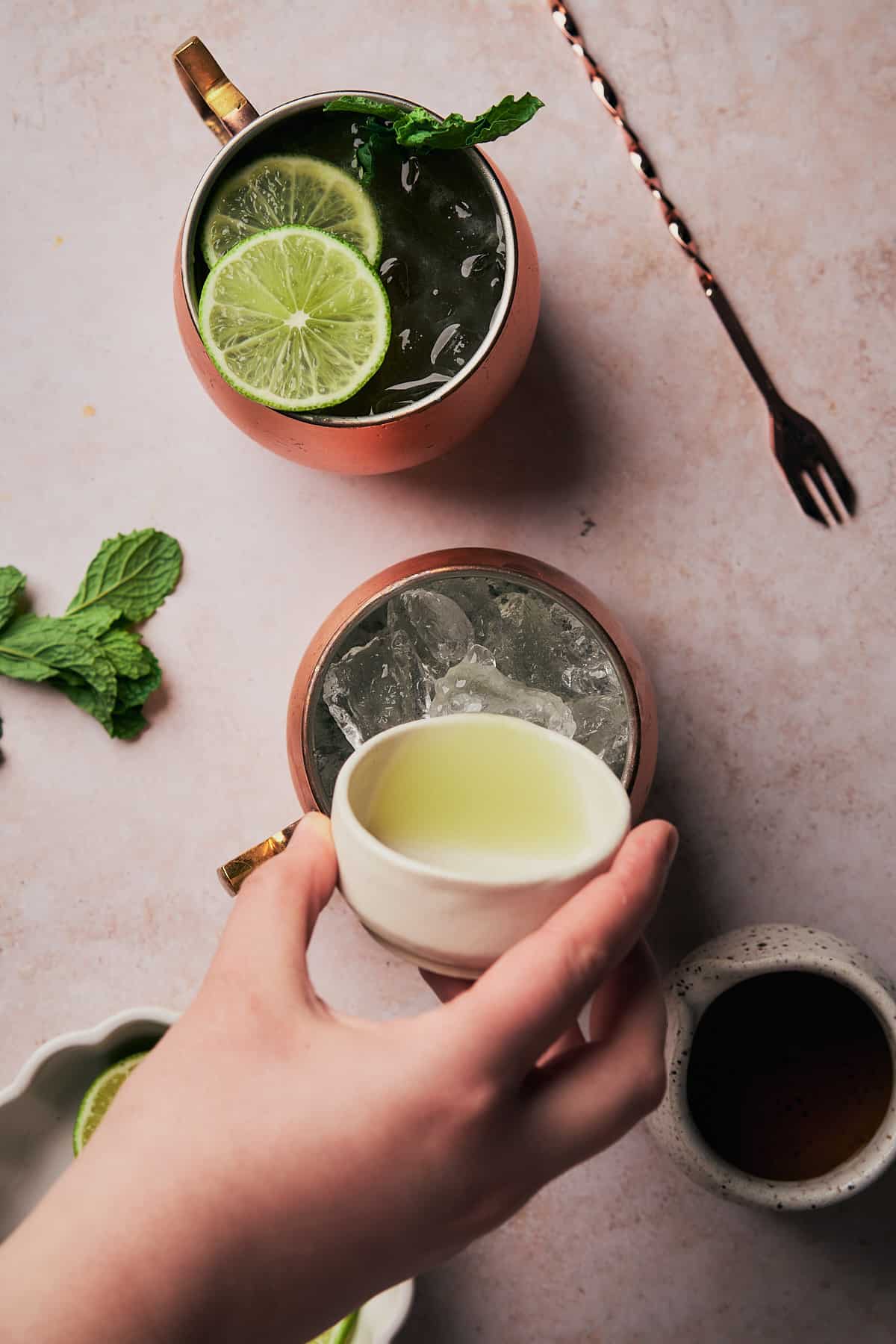 hand pouring fresh lime juice into an ice filled copper mug. 