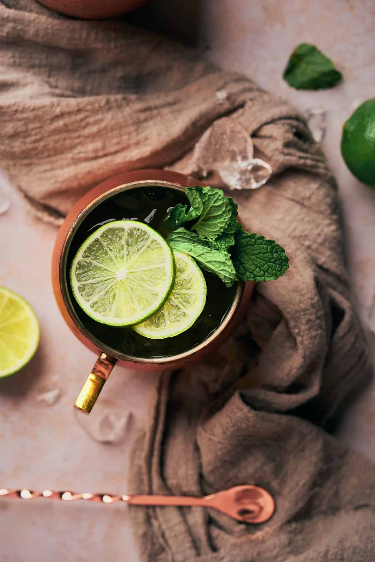 pretty flay lay of a drink with lime slices, fresh mint, and a grey linen napkin underneath. 