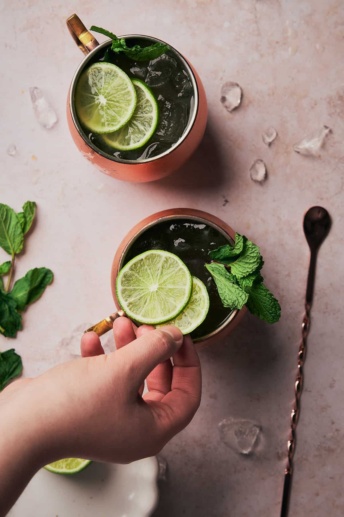 hand placing lime slices on top of a drink in a copper mug. 