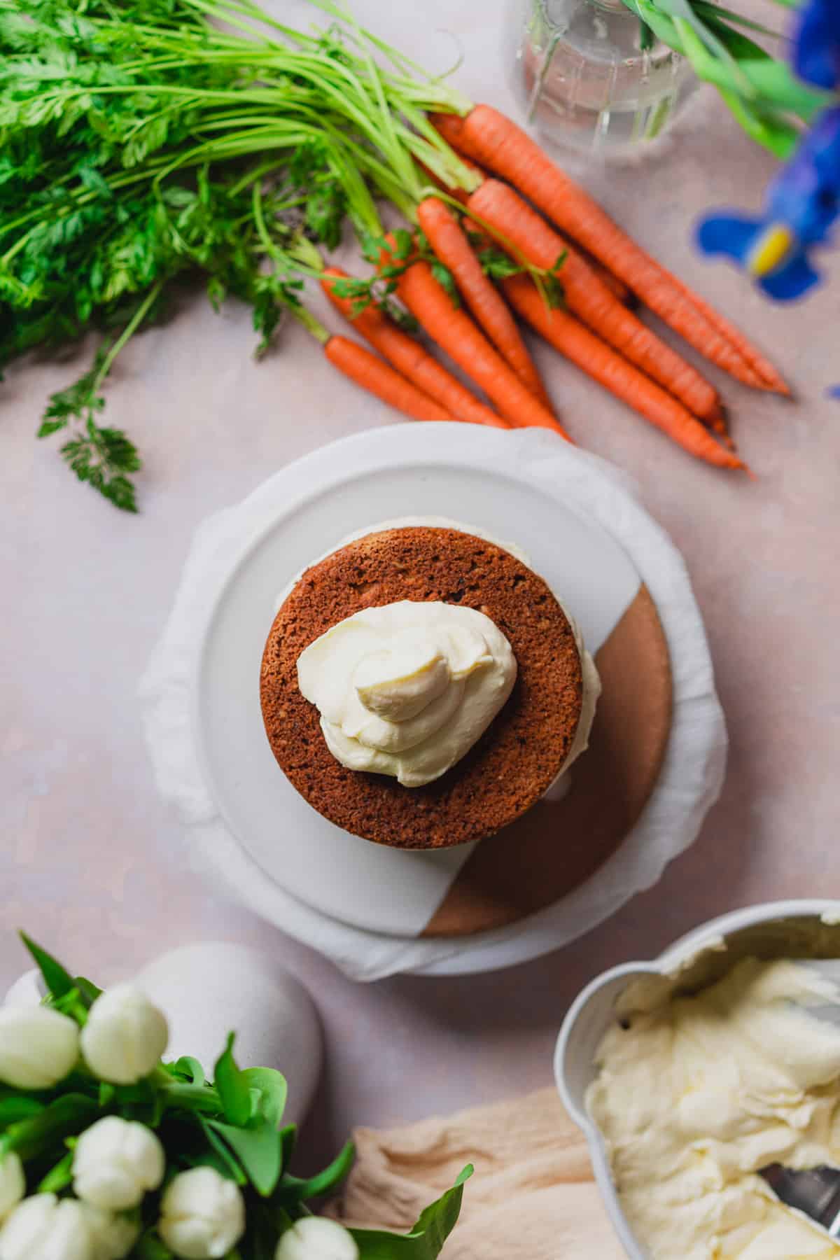 cake layers with large spoonful of cream cheese frosting, and fresh carrots surrounding it. 