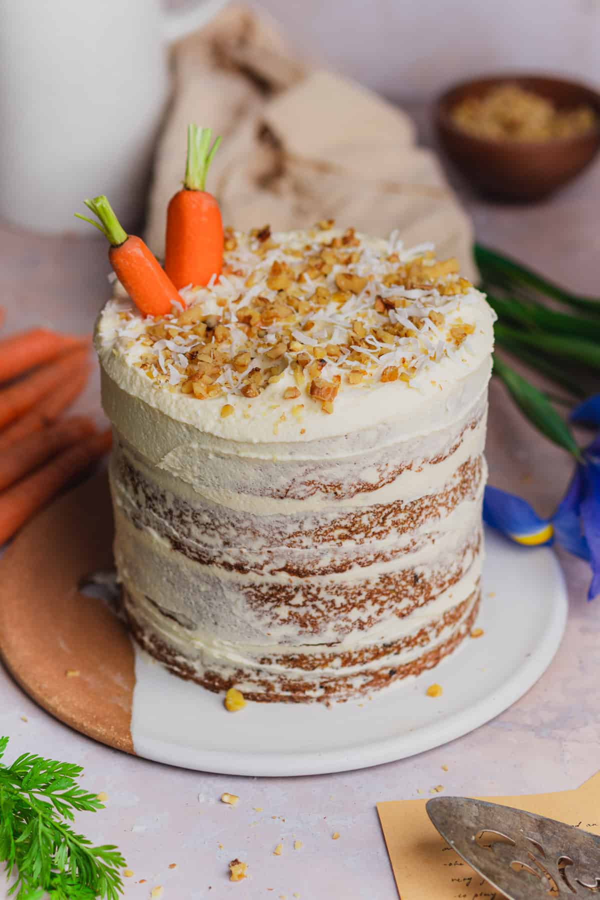 straight on shot of a 4 layer keto carrot cake with fresh carrots, coconut, and walnut. 