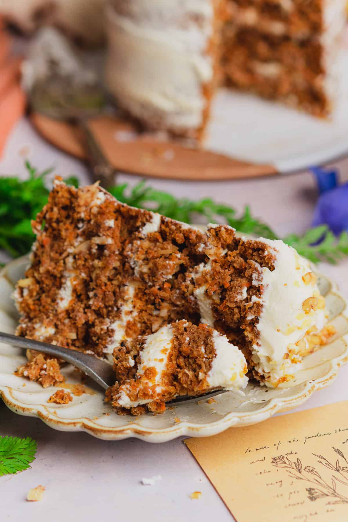 Keto carrot cake slice on a plate with cream cheese frosting, and walnuts. 