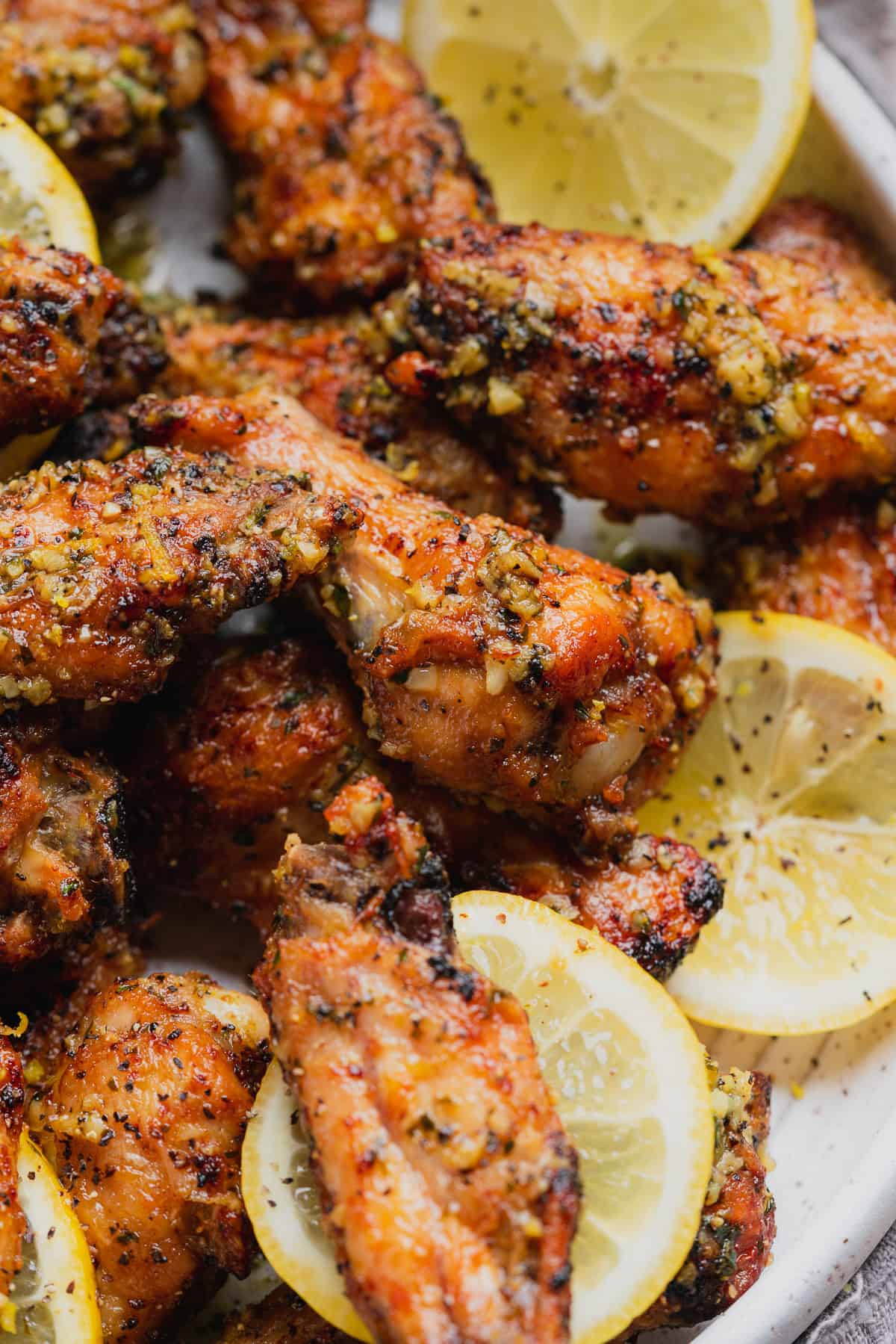 lemon pepper wings cooked in the air fryer with lemon rounds on a plate. 
