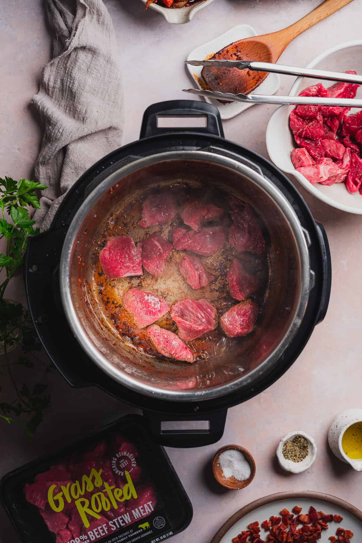 cooking beef stew meat in an Instant pot with parsley nearby.