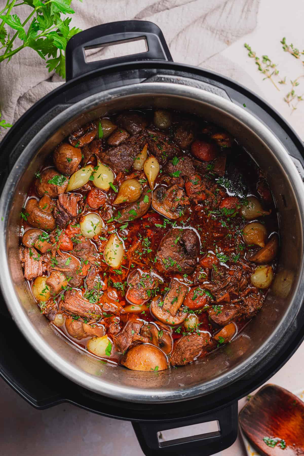 beef bourguignon in a pressure cooker topped with fresh parsley and thyme. 