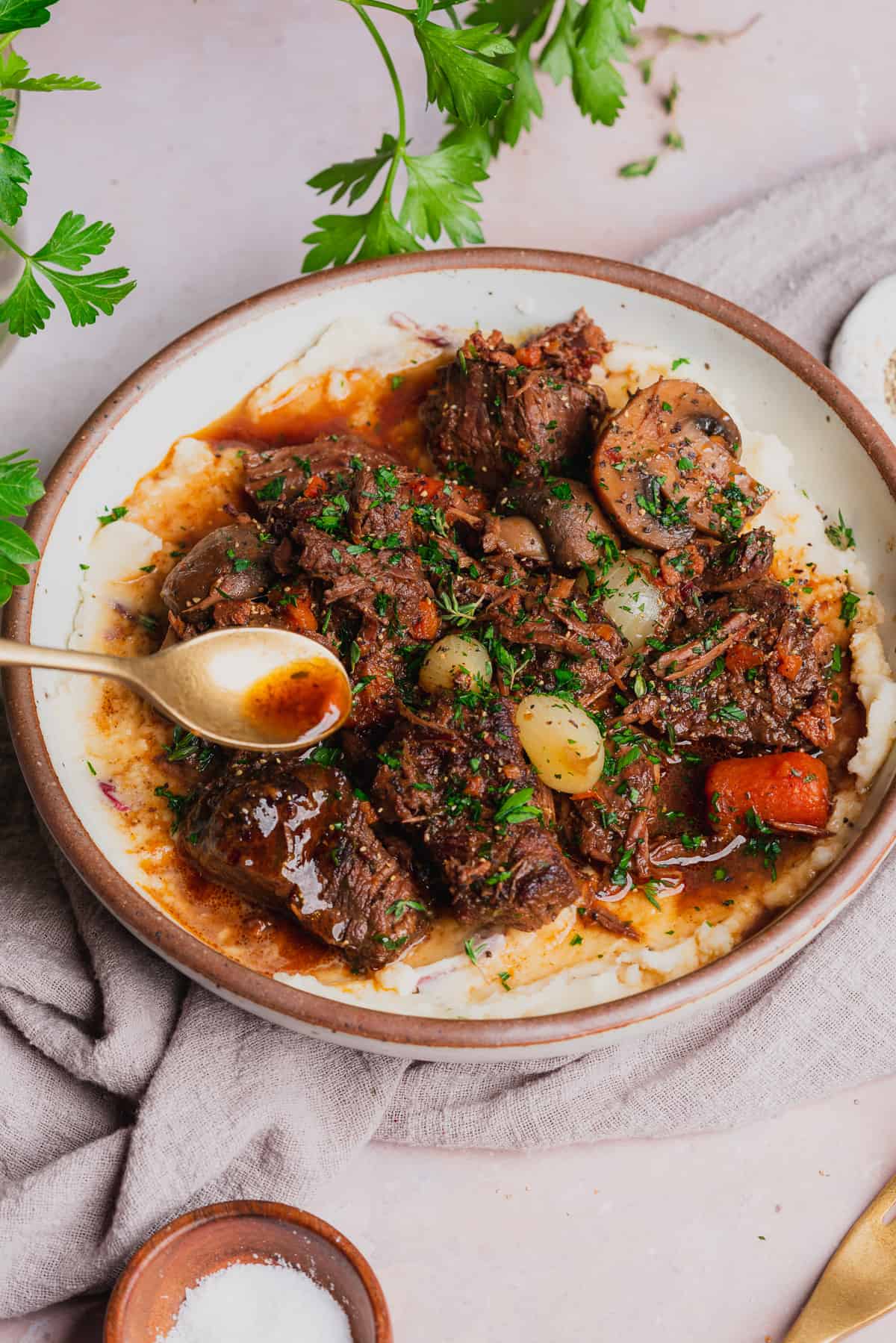 drizzling red wine gravy over top of a bowl of pressure cooker beef bourguignon served over mashed potatoes. 