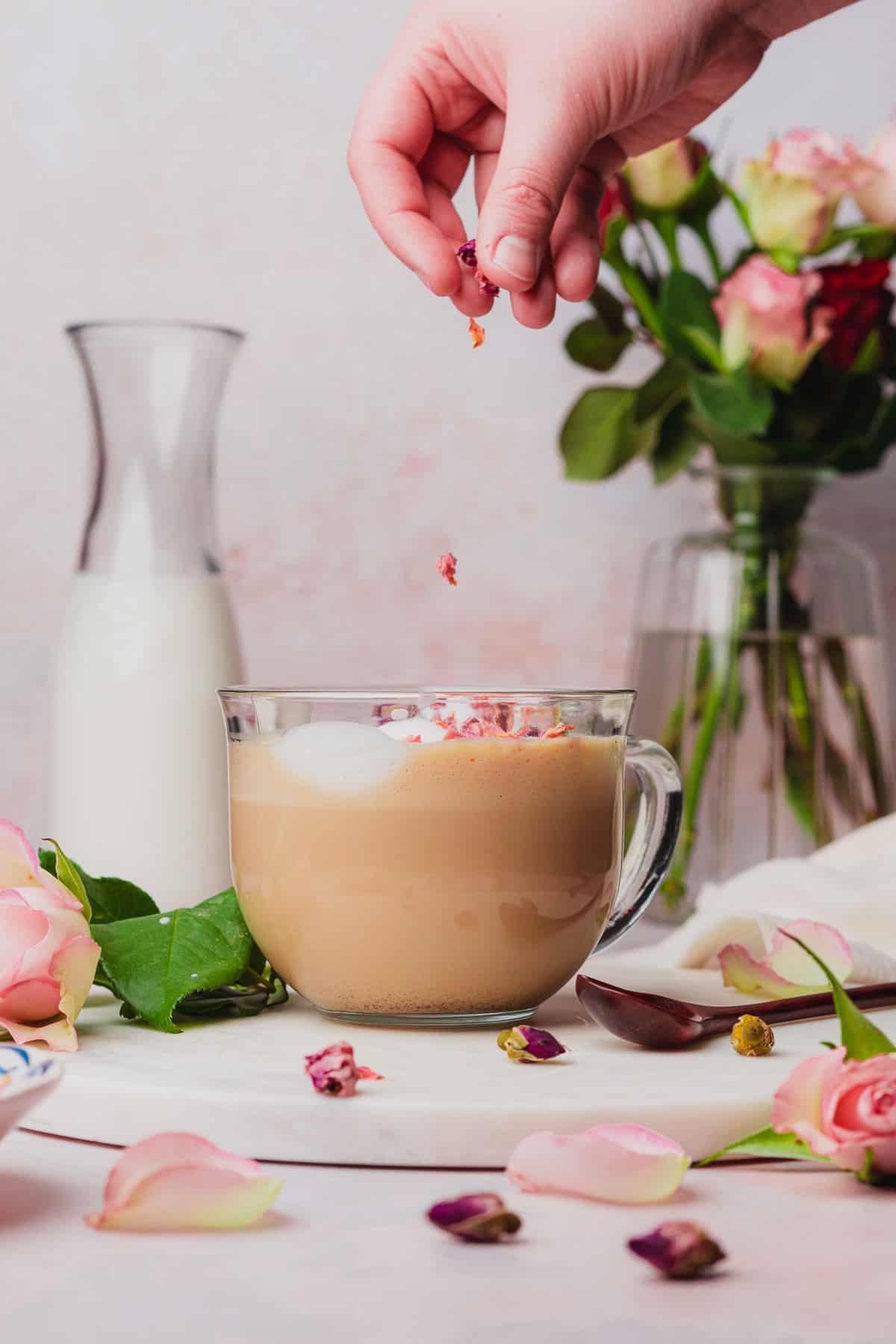 hand sprinkling rose petals on top of a rose latte.