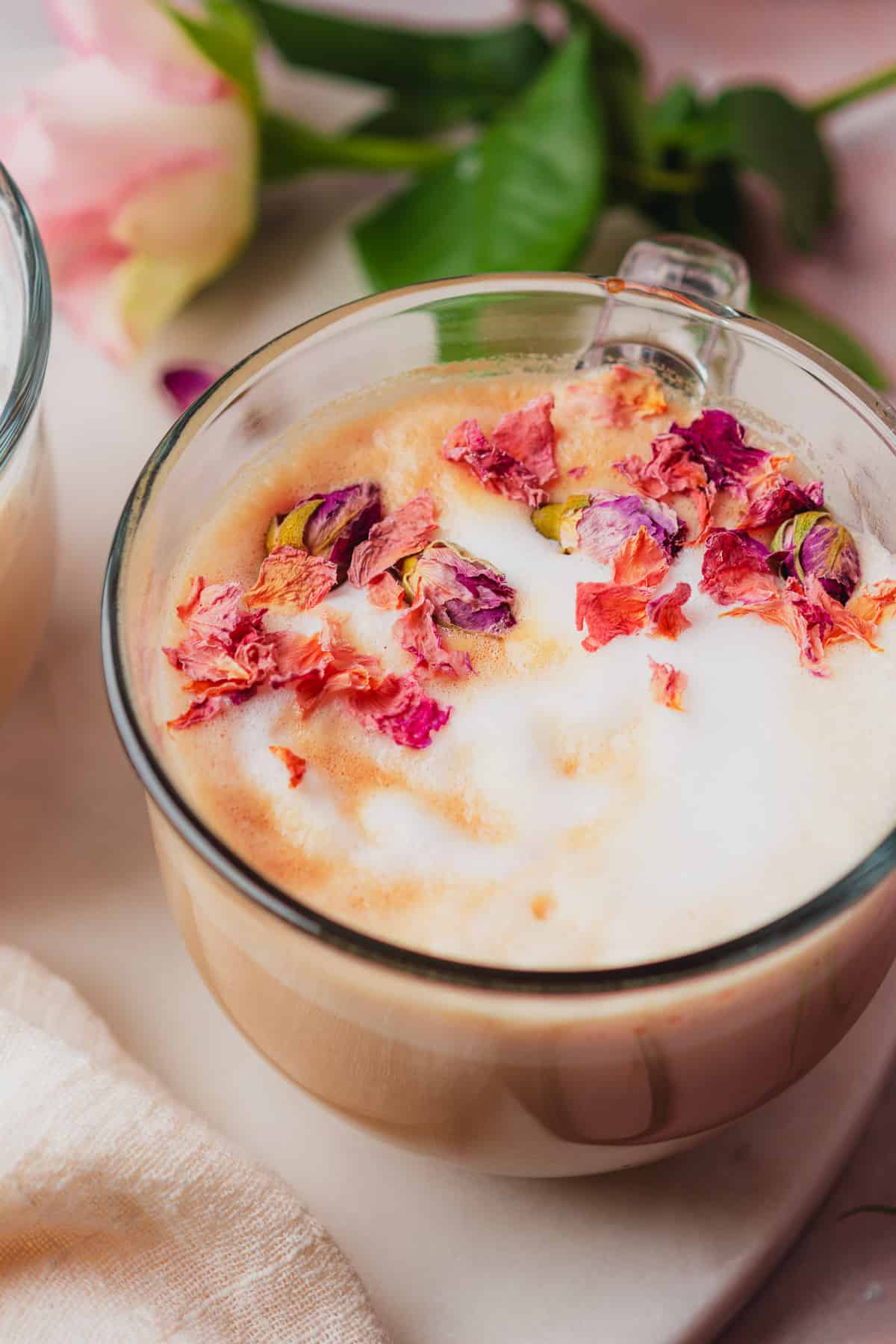 close up shot of a rose latte with edible rose petals and real roses in the background. 