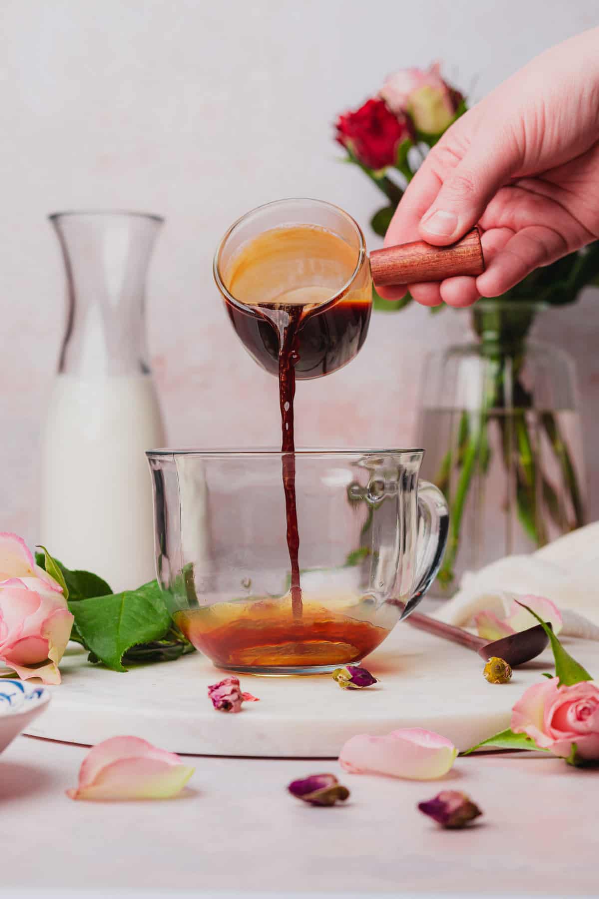 hand pouring espresso into a large coffee mug surrounded by flowers. 
