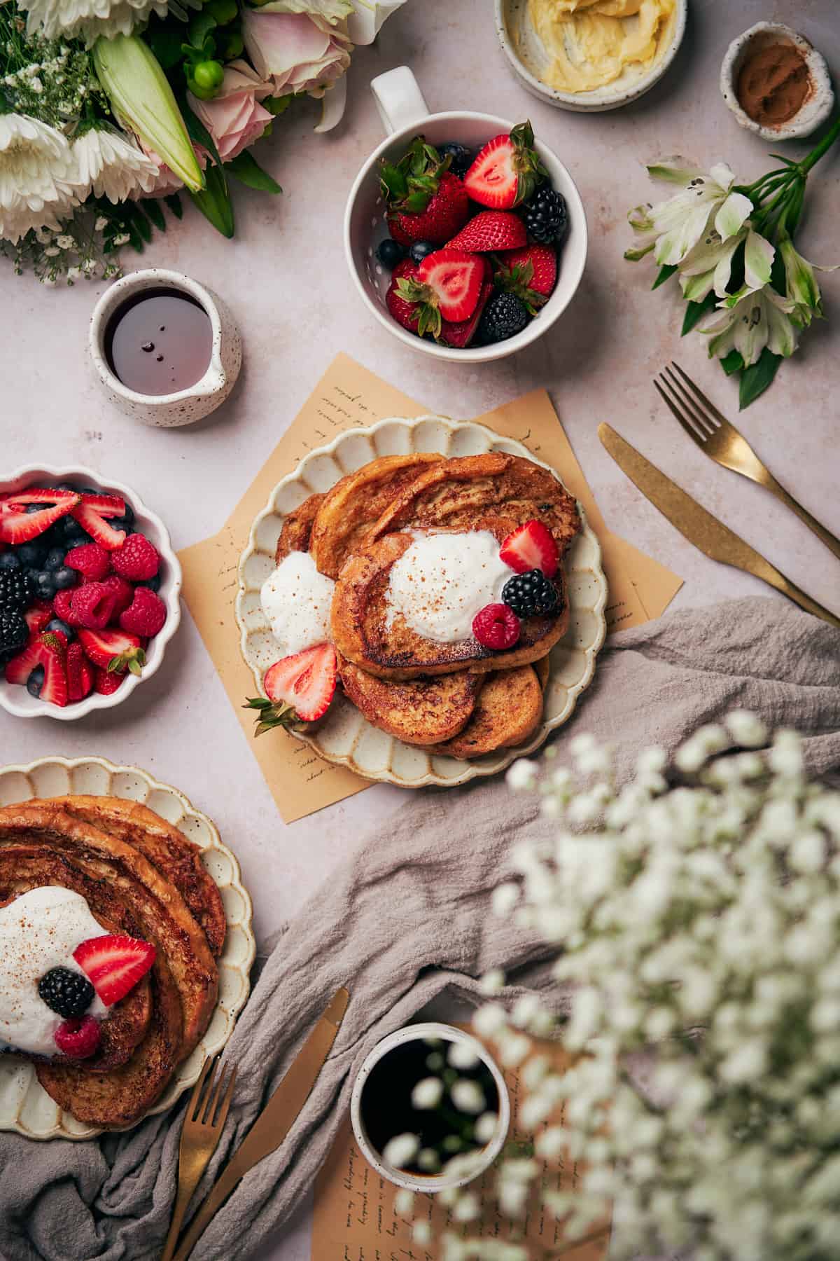 beautiful flat lay of sourdough french toast with berries, and flowers surrounding everything. 