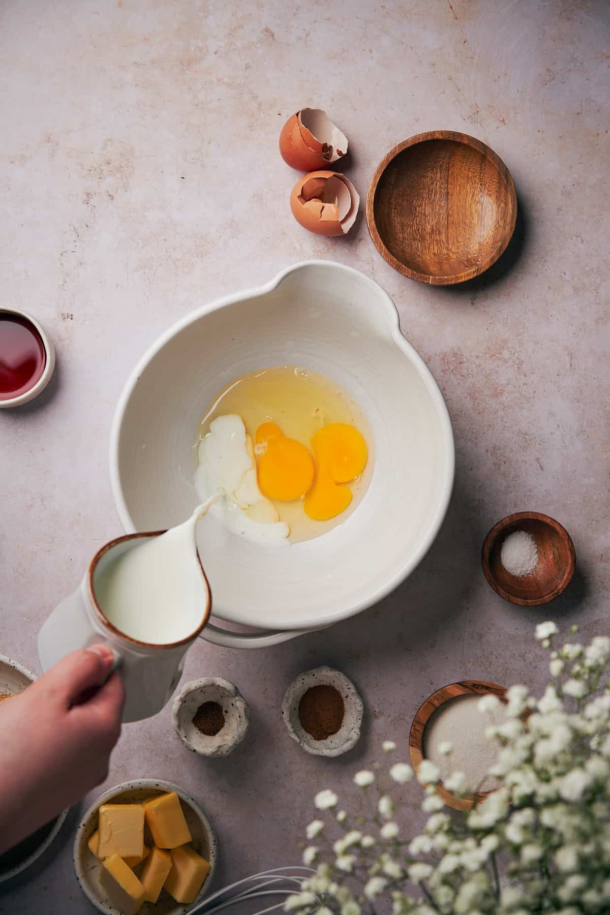 hand pouring milk into a ceramic mixing bowl with eggs.