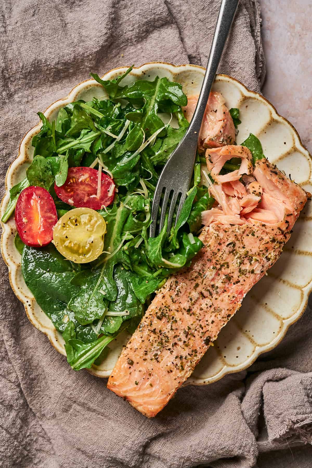 arugula spinach salad with tomatoes on a plate with a slice of salmon. 