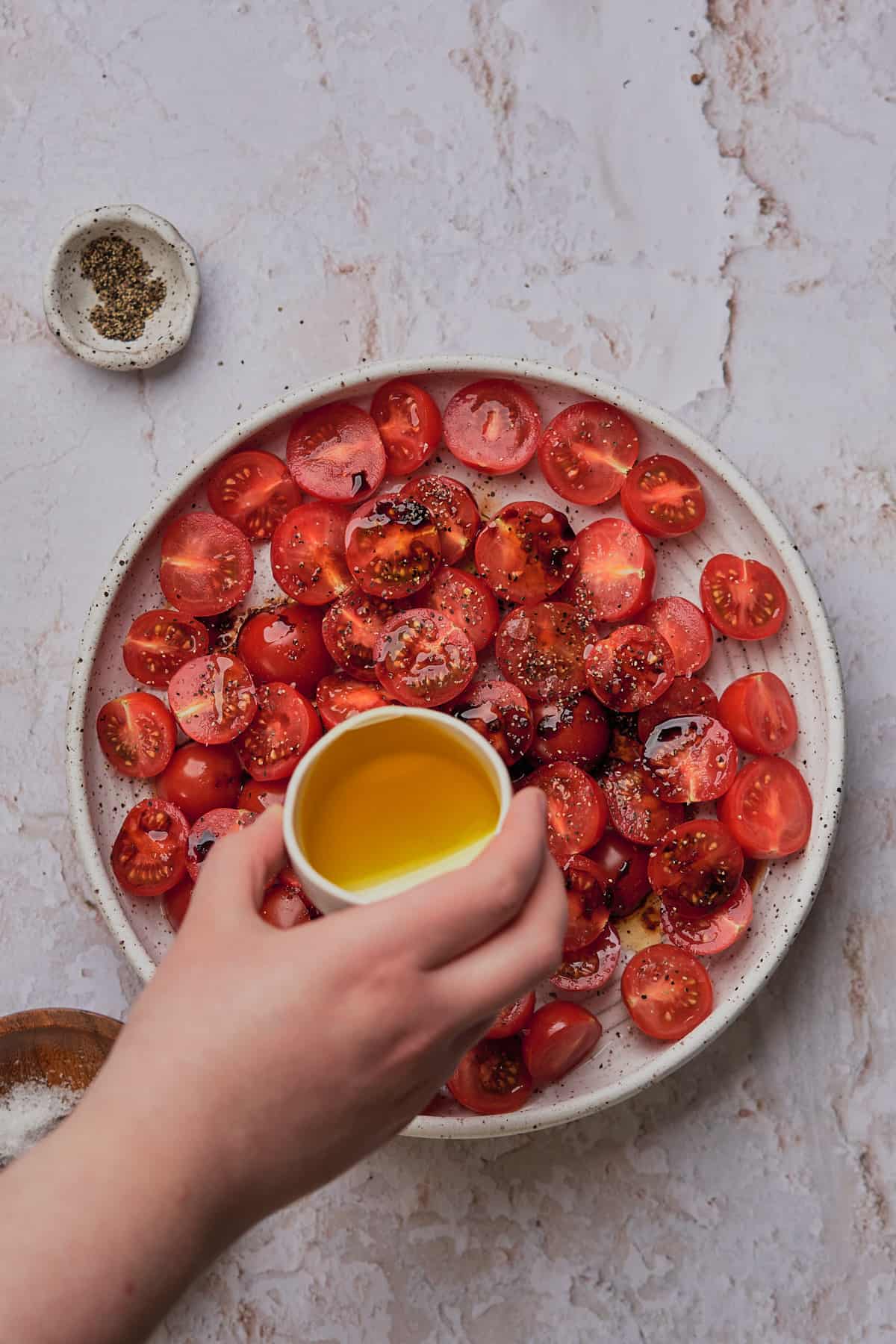 hand drizzling olive oil over top of tomatoes. 