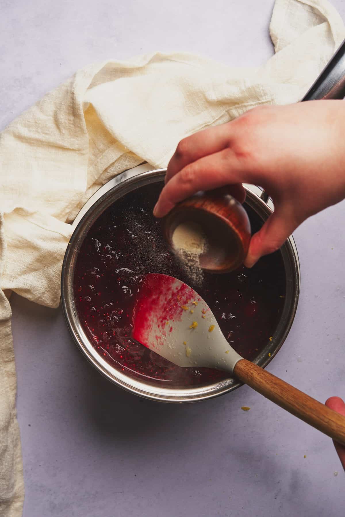 hand sprinkling xanthan gum into a saucepan of cranberry sauce. 